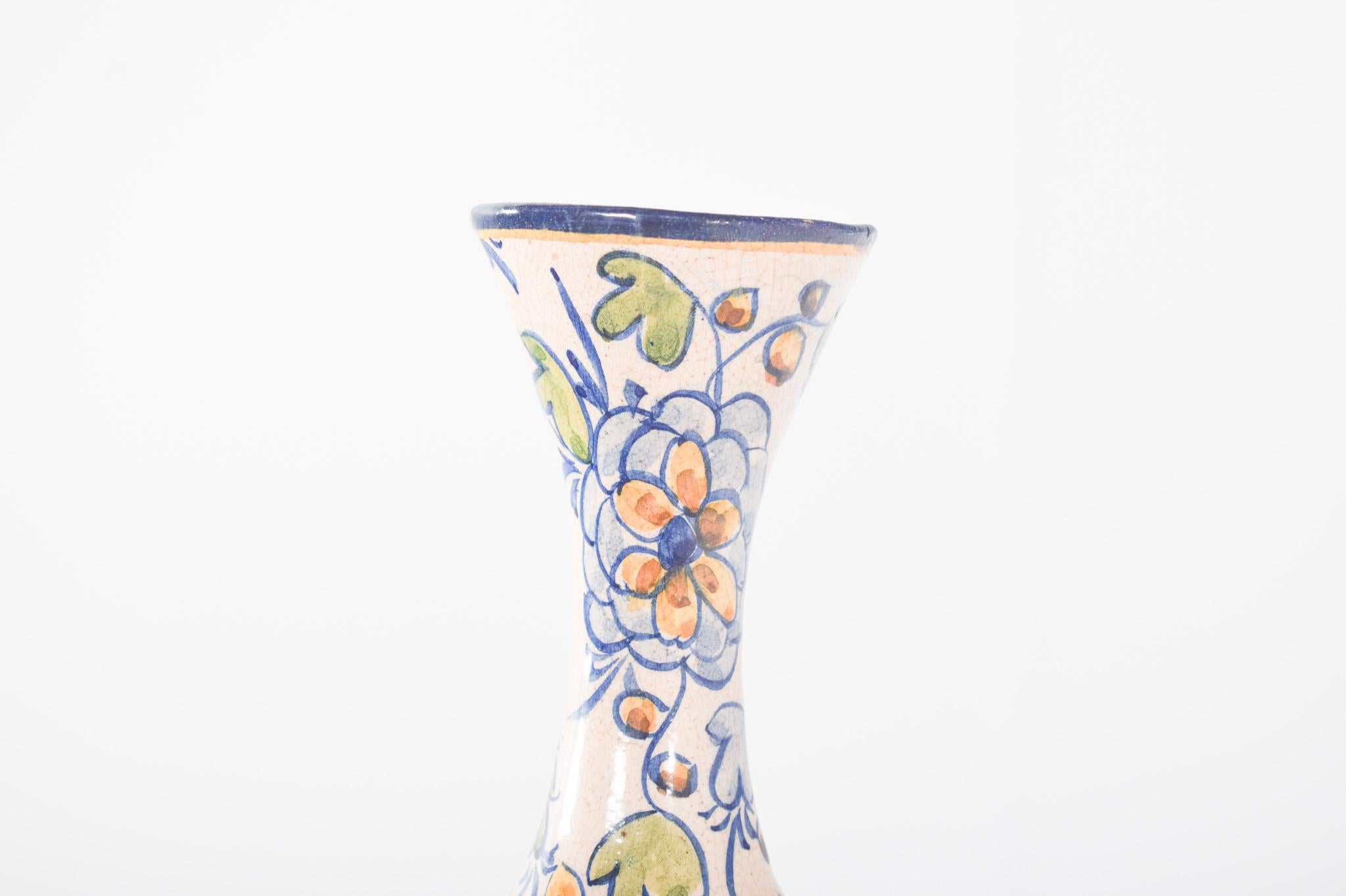 Vaso di terracotta Alcobaça. Svasato alla base e con un collo lungo e stretto che si apre leggermente in alto. Lo sfondo è bianco, con un motivo floreale dipinto nei toni del blu, dell'arancio e del verde. I fiori sono delineati in blu scuro e