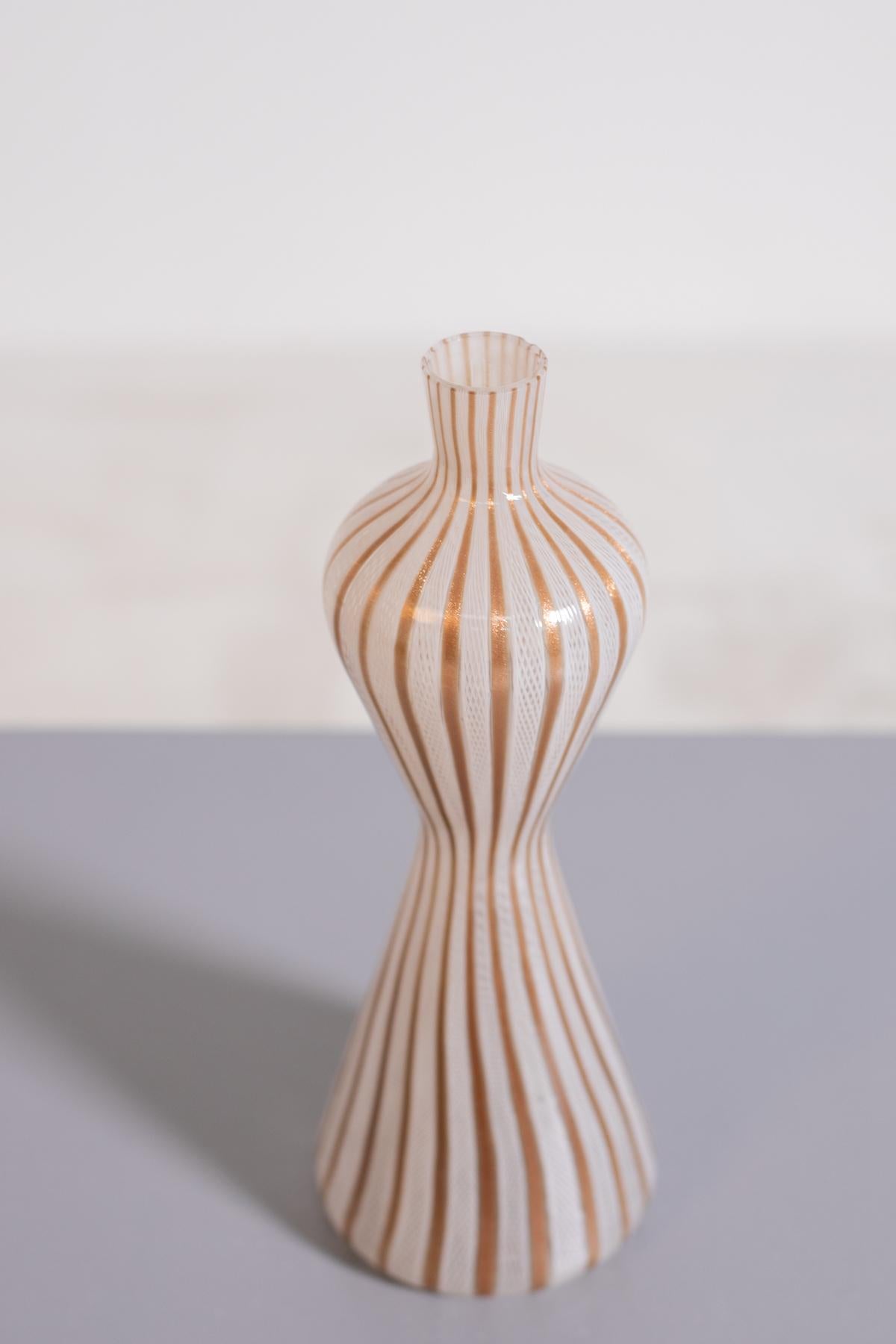 Glass with gold coloured ribbon with vertical lines inside transparent glass reticello technique, work of the master Venini. The elegant tall, hourglass-shaped vase has a narrow neck with a flat, rounded top. Signed, 1950s

Dimensions:
Height 30