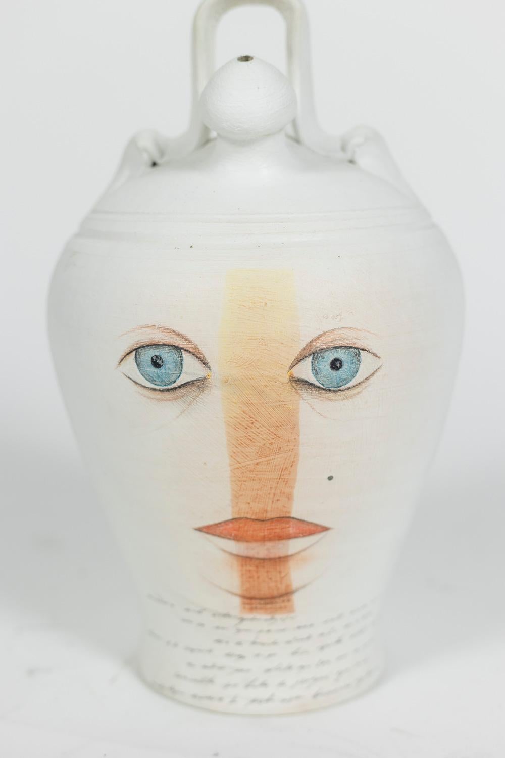 Painted terracotta vase, surreal style and round shape. Face in blue and orange tones on an background in white color.

Contemporary work.