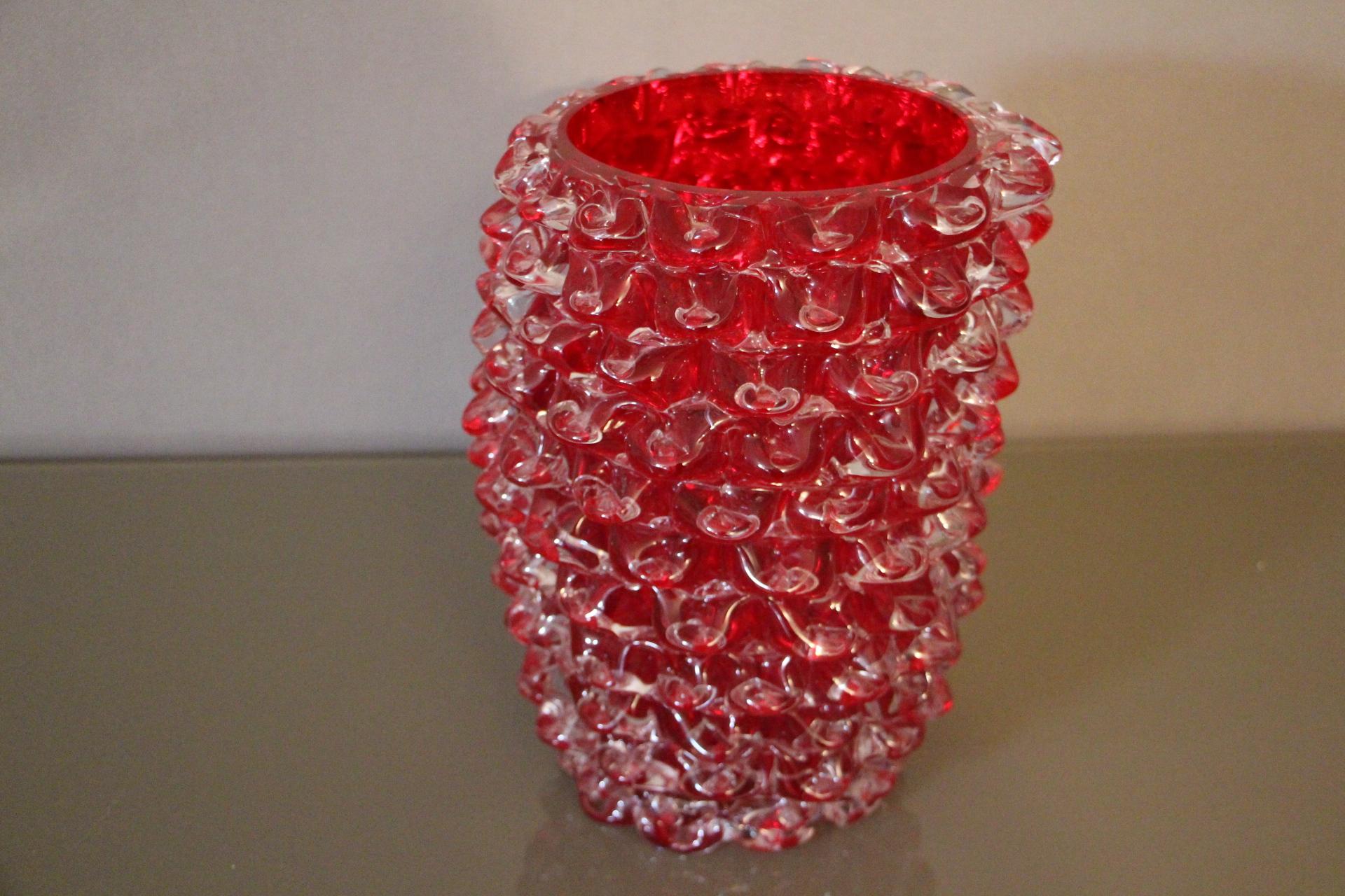 Eine wunderschöne Vase aus klarem und tiefrotem mundgeblasenem Murano-Glas, handdekoriert mit der Technik rostrato: einzeln in Relief gezogene Glaszacken.
Dickwandiges Mantelglas erzeugt eine Menge schillernder Reflexe.
Signiert auf der
