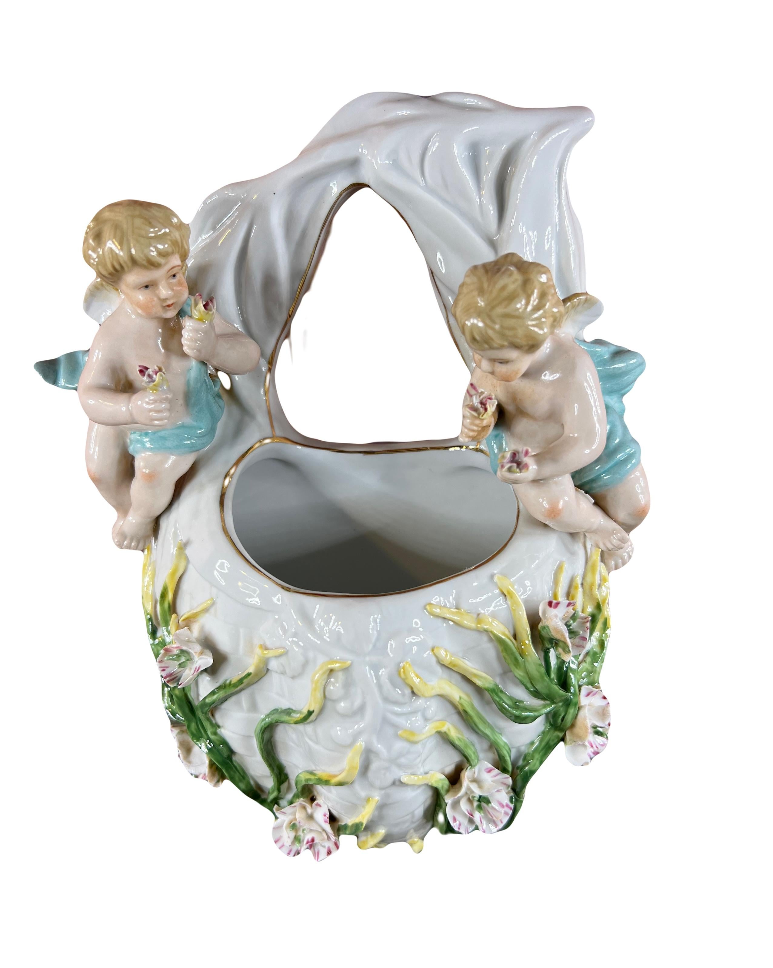 Cette magnifique pièce de décoration murale présente un vase d'applique ou bouquetière en porcelaine de Meissen. Deux charmants chérubins tiennent des bouquets de fleurs délicates dans leurs mains, ajoutant une touche angélique à l'ensemble. Ils