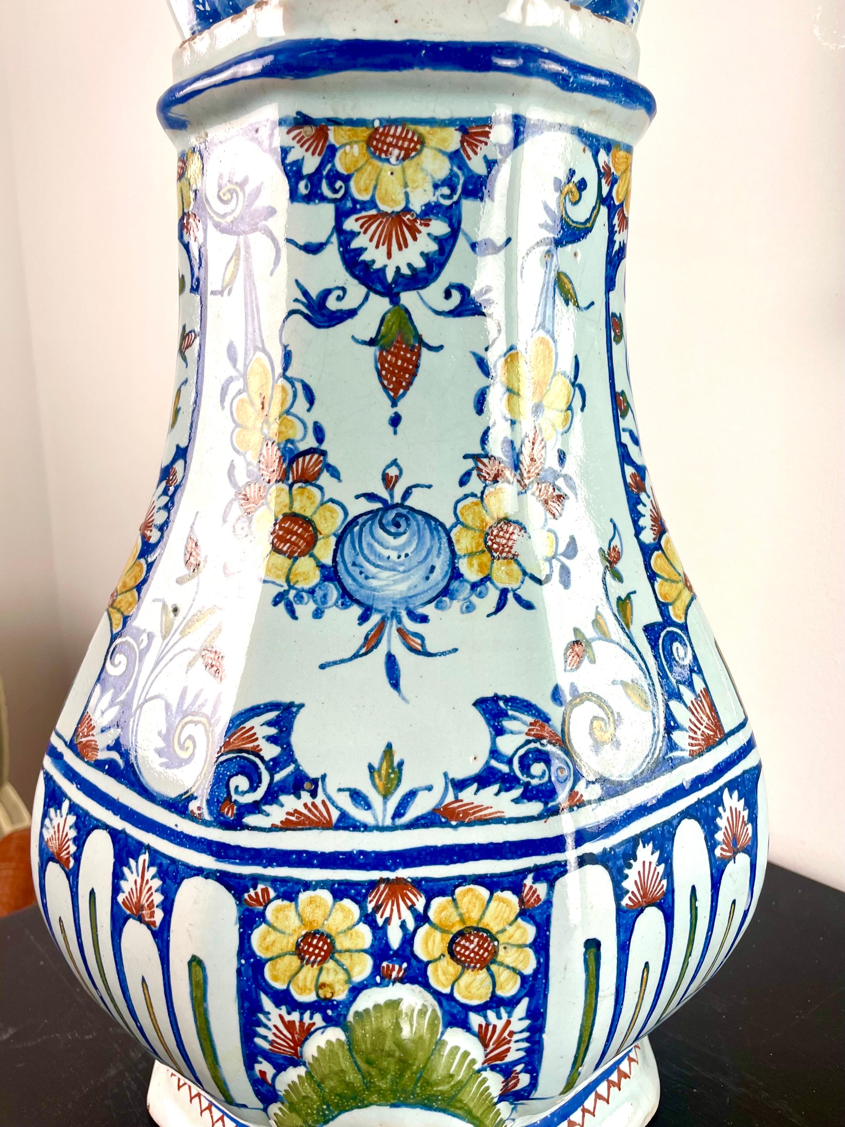 Pretty earthenware wall fountain in the shape of a baluster with polychrome decoration in blue, yellow, red and white, surmounted by a shell flanked by dolphins. The decoration of the fountain, flower pot or vase represents a shell as well as two