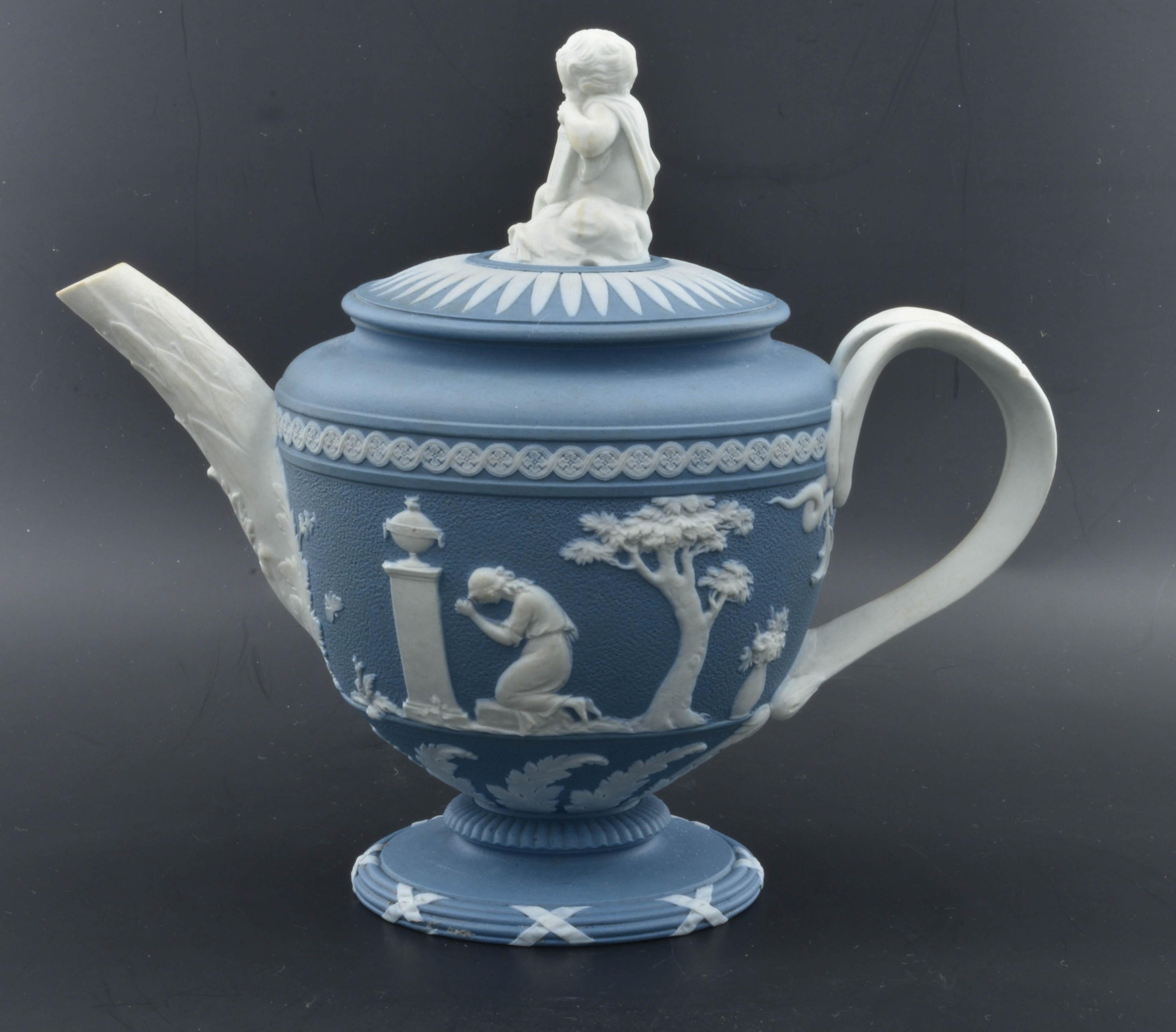 A shield-shaped teapot, decorated with typical reliefs including Charlotte at the Tomb of Werther and Domestic Affection, both designed by Lady Templetown. Cupid with his quiver forms the finial, and a leaf-wrapped spout is an attractive