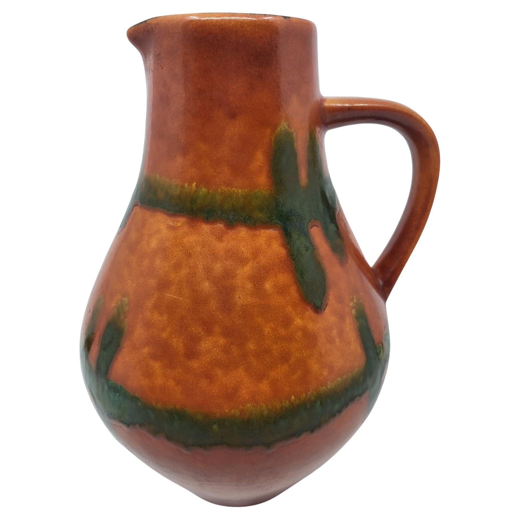 Ce vase vintage en céramique, fabriqué en Allemagne de l'Ouest dans les années 1970, est une pièce emblématique du design de cette époque. Avec sa hauteur de 26 cm, il attire l'attention par son éclatante couleur orange, ornée d'un décor vert qui