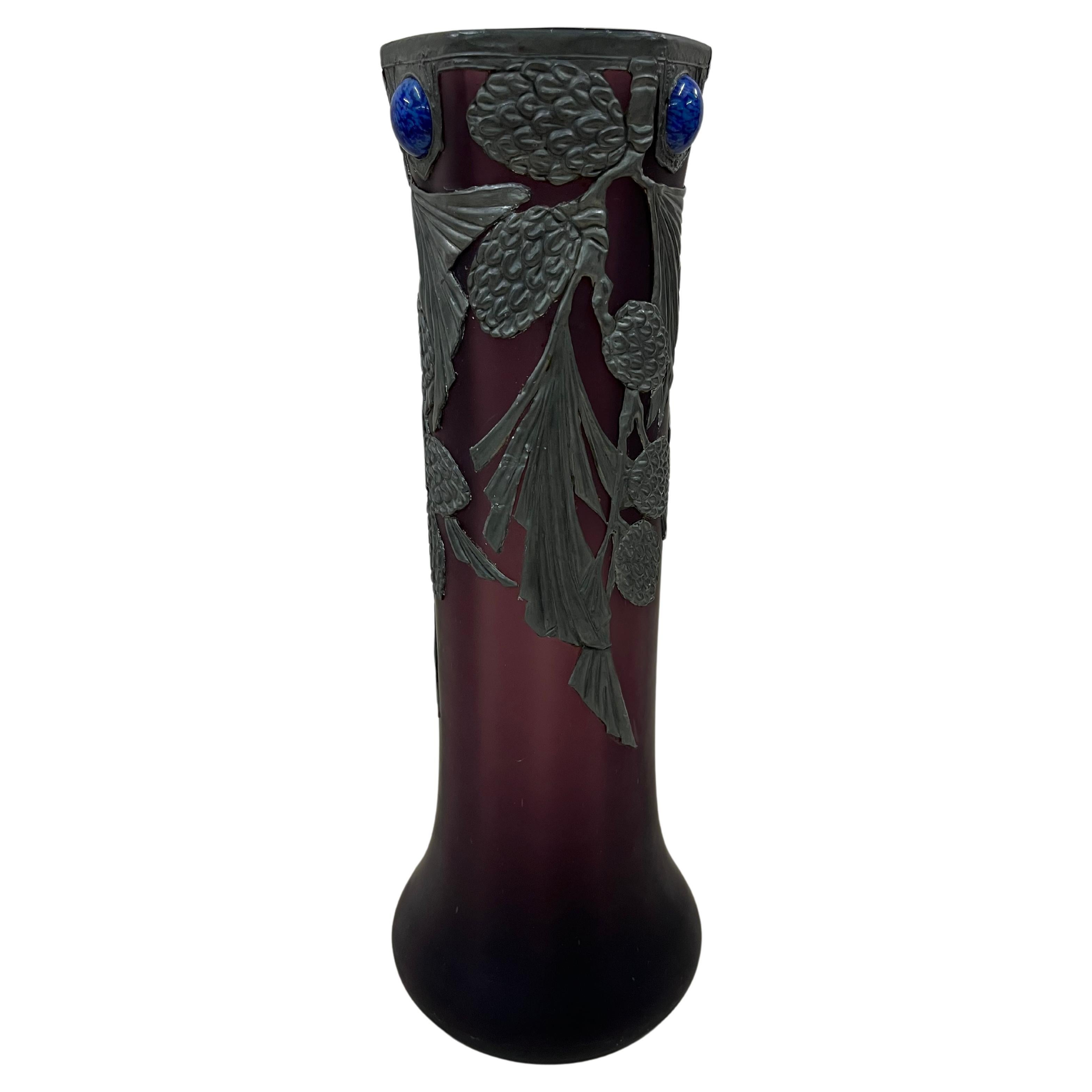 Wonderful dreamy vase, an original from the art nouveau period, made around 1910 in probably France (or Belgium), with floral metal mounting and glass gemstones.

The vase is made of purple glass, with a round base, a thinned body that then ends in