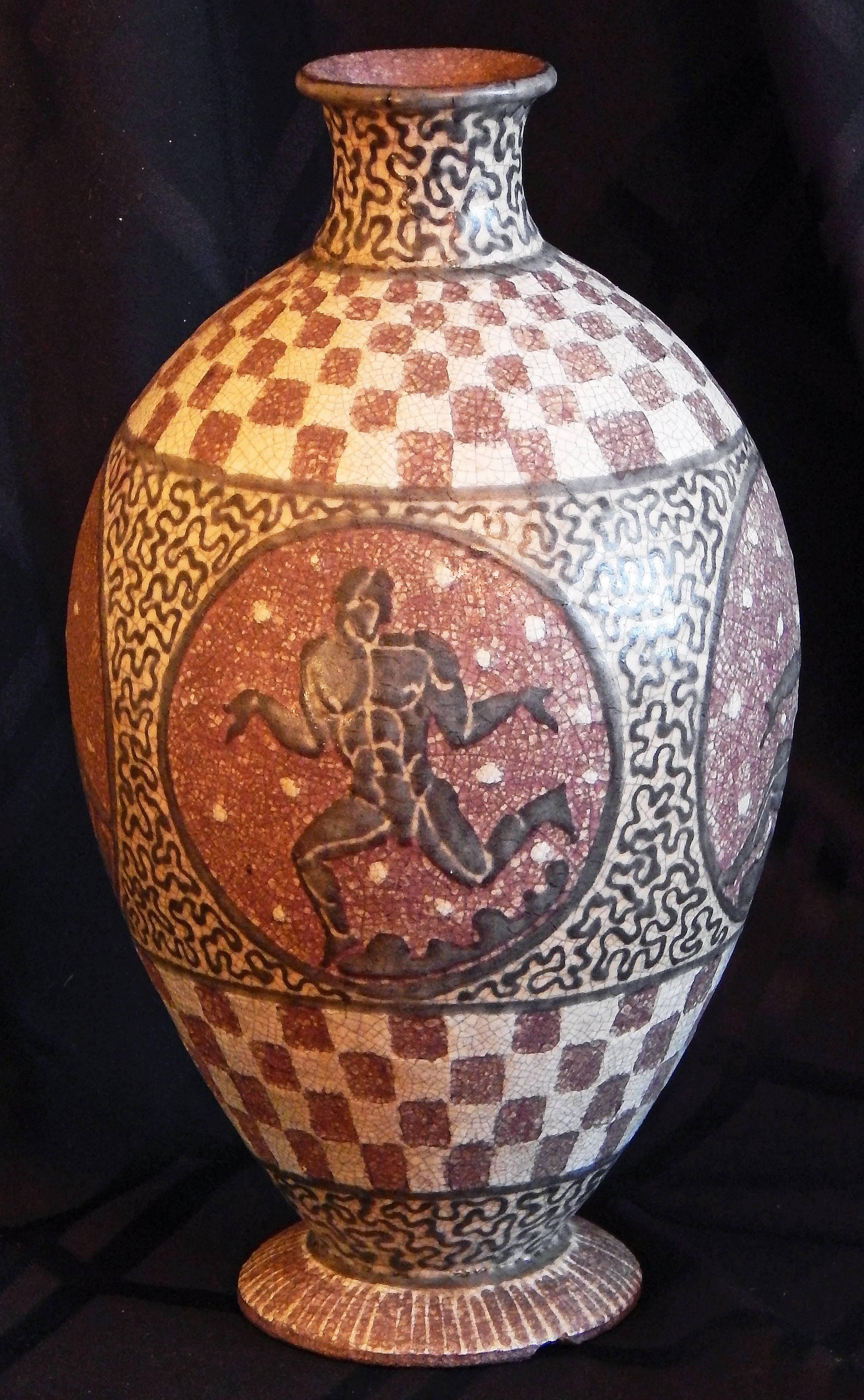 Riccamente smaltato nei toni del marrone rubino, dell'avorio e del cioccolato scuro, questo splendido vaso di Jean Mayodon presenta una serie di medaglioni con figure maschili classiche nude in varie pose. Una figura è raffigurata mentre corre con