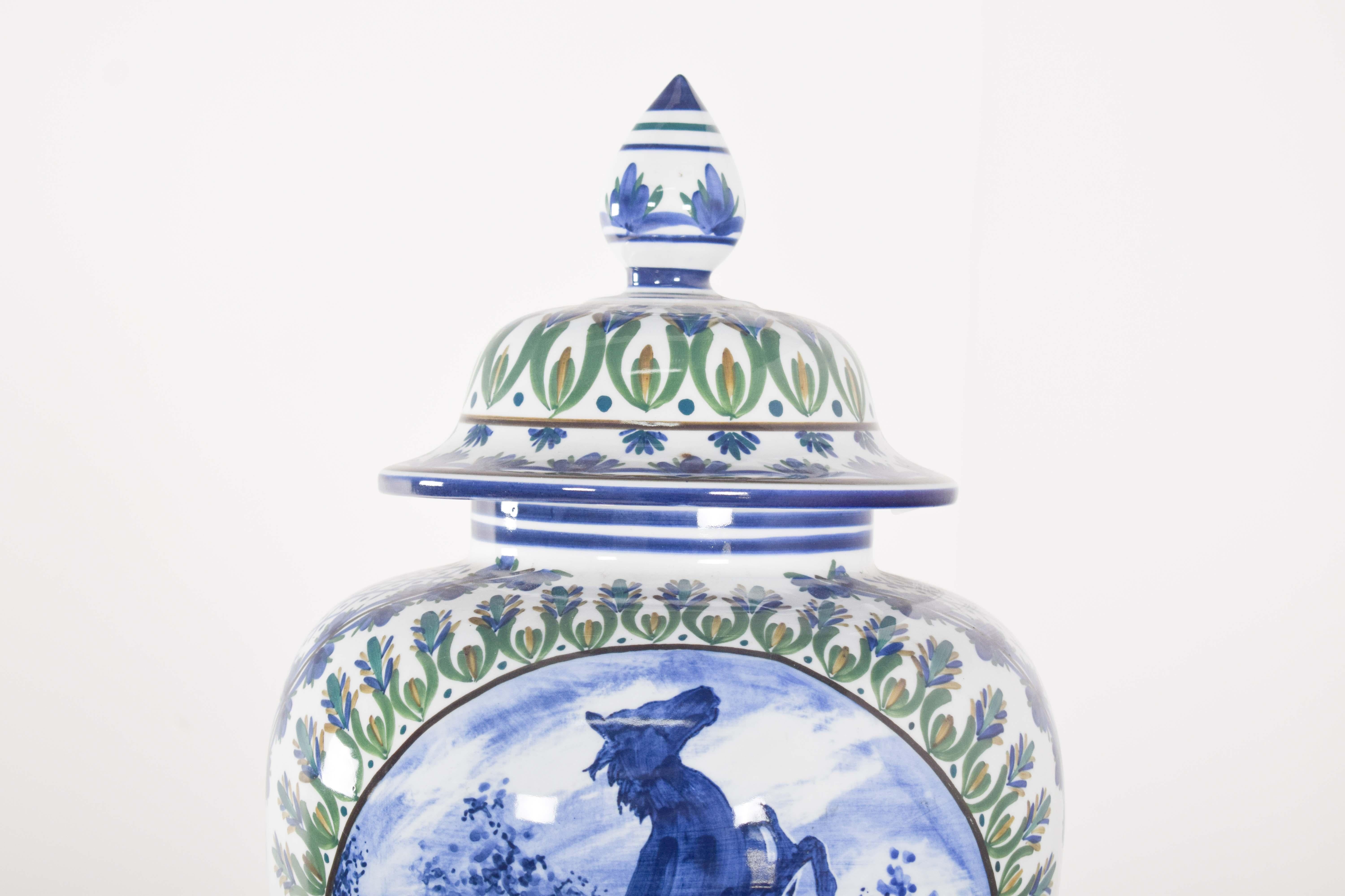 Jarrón con tapa de porcelana Alfe. La porcelana de Alfe, conocida por su tradición y calidad en Portugal, destaca en esta pieza por la armoniosa combinación de tonos azules y verdes y la representación realista de un paisaje campestre con un caballo