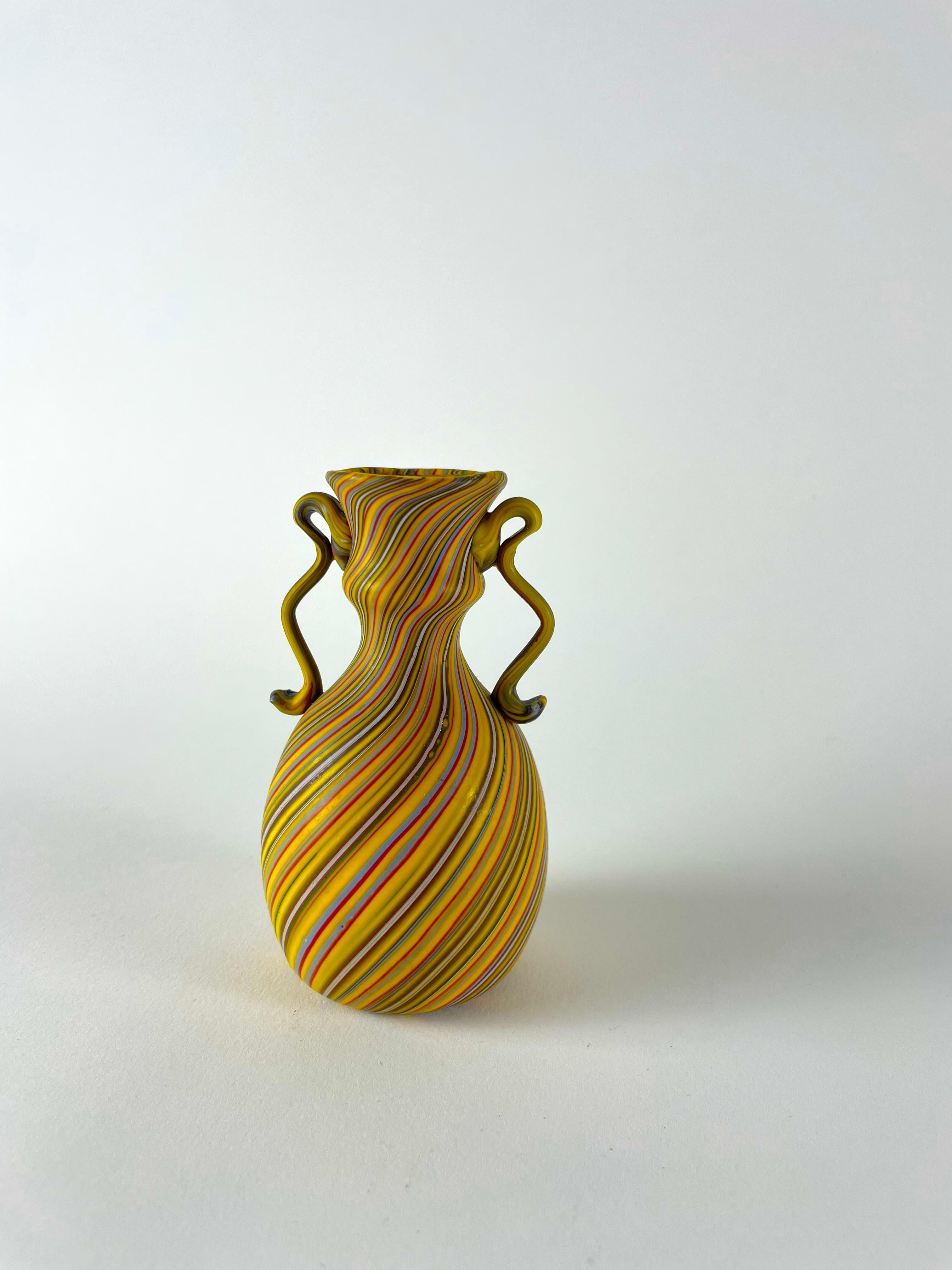 Voici le Vaso a canne, un petit trésor qui incarne l'incroyable savoir-faire de Murano. Ce vase exquis est méticuleusement fabriqué à la main selon une technique unique, avec de petites cannes de verre disposées selon un motif régulier et