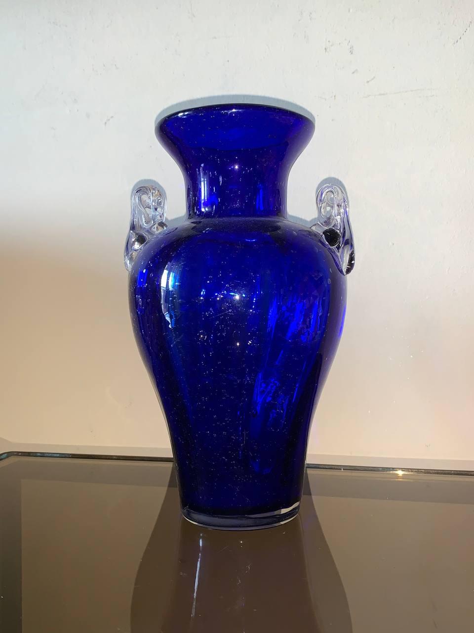 Das auffallend kobaltblaue Muranoglas zeigt eine raffinierte Glockenform, die mit eleganten, kontrastierenden, klaren Muranoglasgriffen verziert ist. Diese luxuriöse Kombination von Farben und Formen fängt die Essenz des modernen Stils der