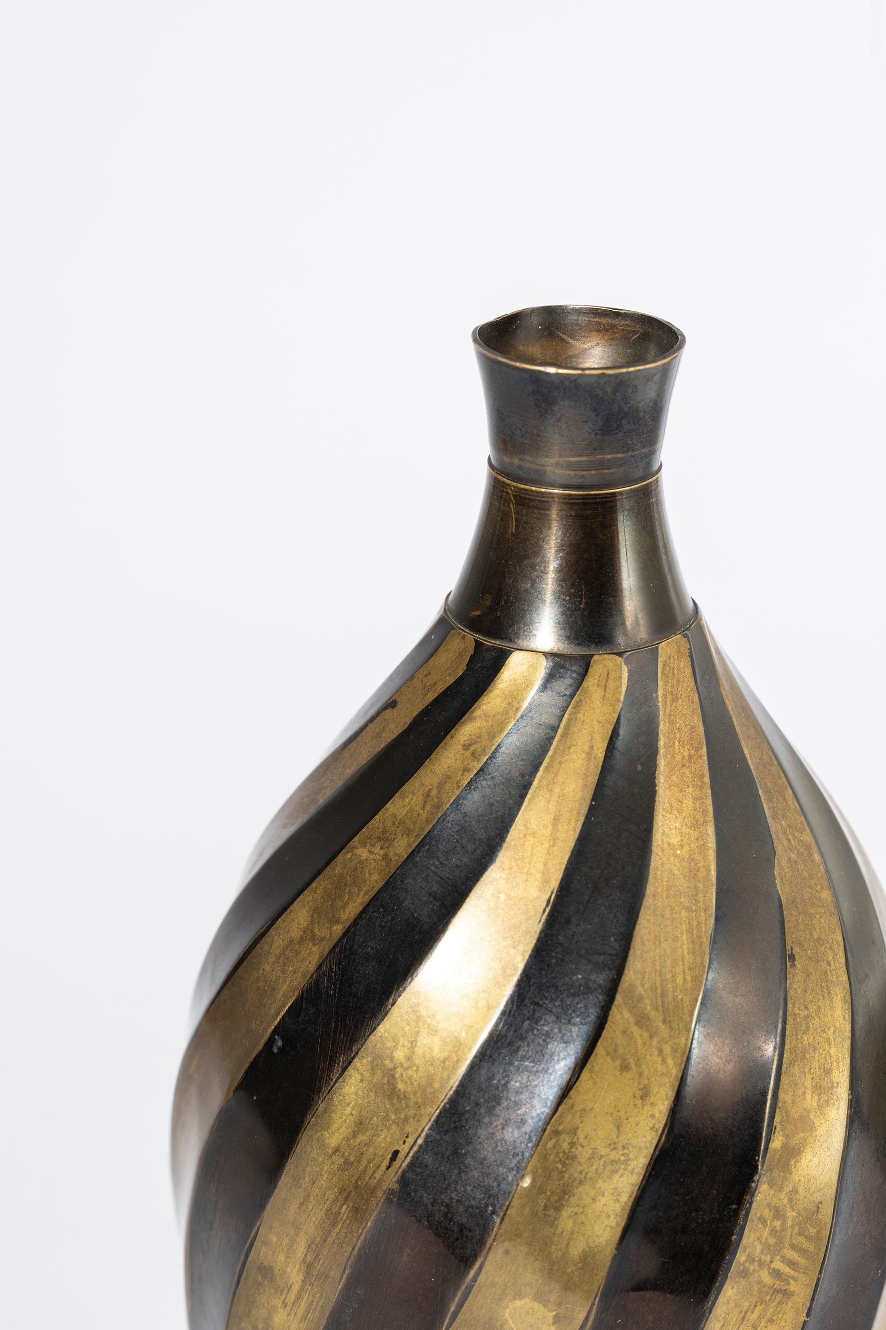 Brass vase, embossed, with alternating lozenge decoration enameled in black tone. The shape and workmanship of the geometric embossing give the vase the strength and dynamism of the deco style. 