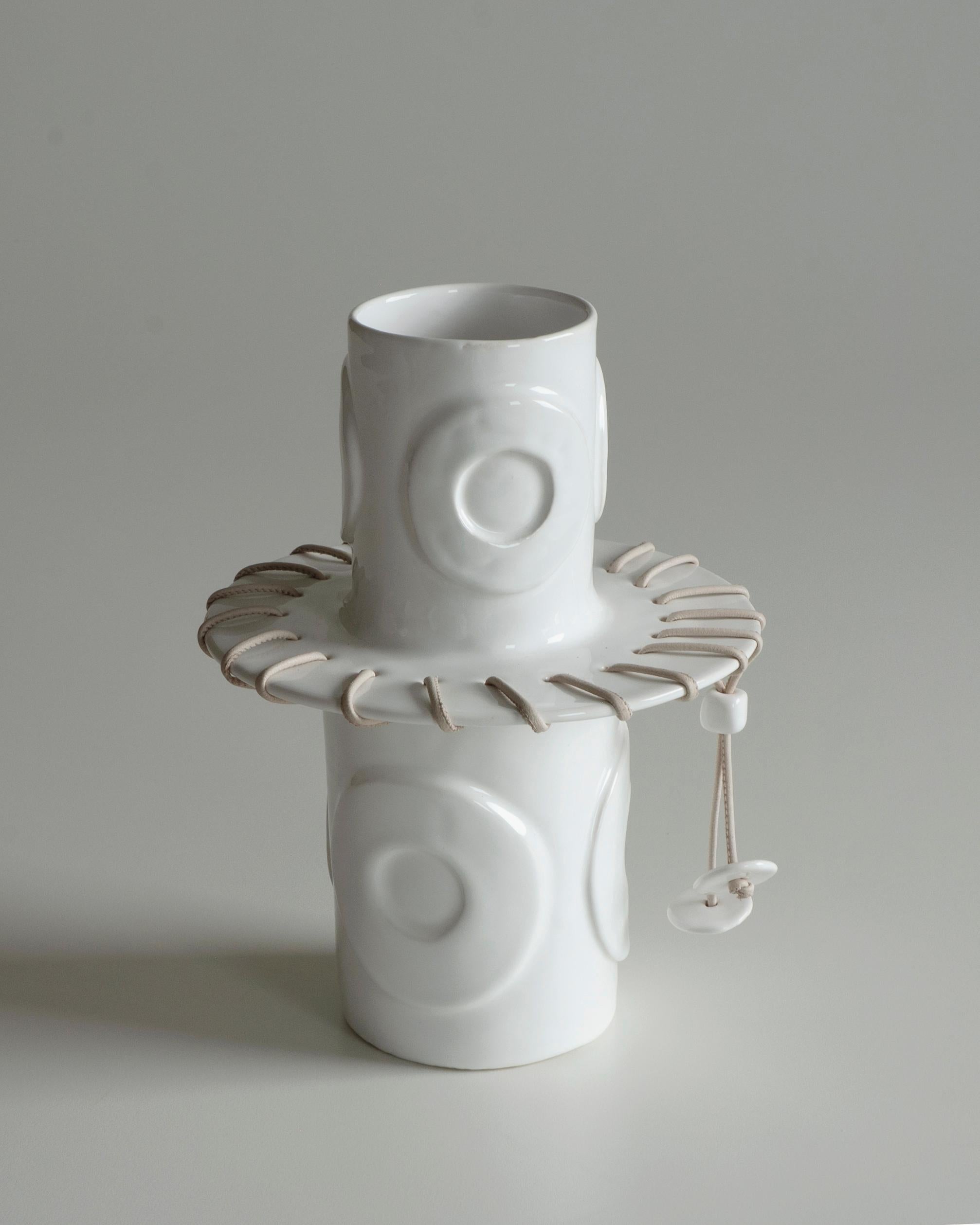 White ceramic vase with decorative relief details. La smaltatura a immersione  blends harmoniously with the decorative details, creating a contrast that makes it unique. The leather drawstring detail represents the seam,  elemento ricorrente nel
