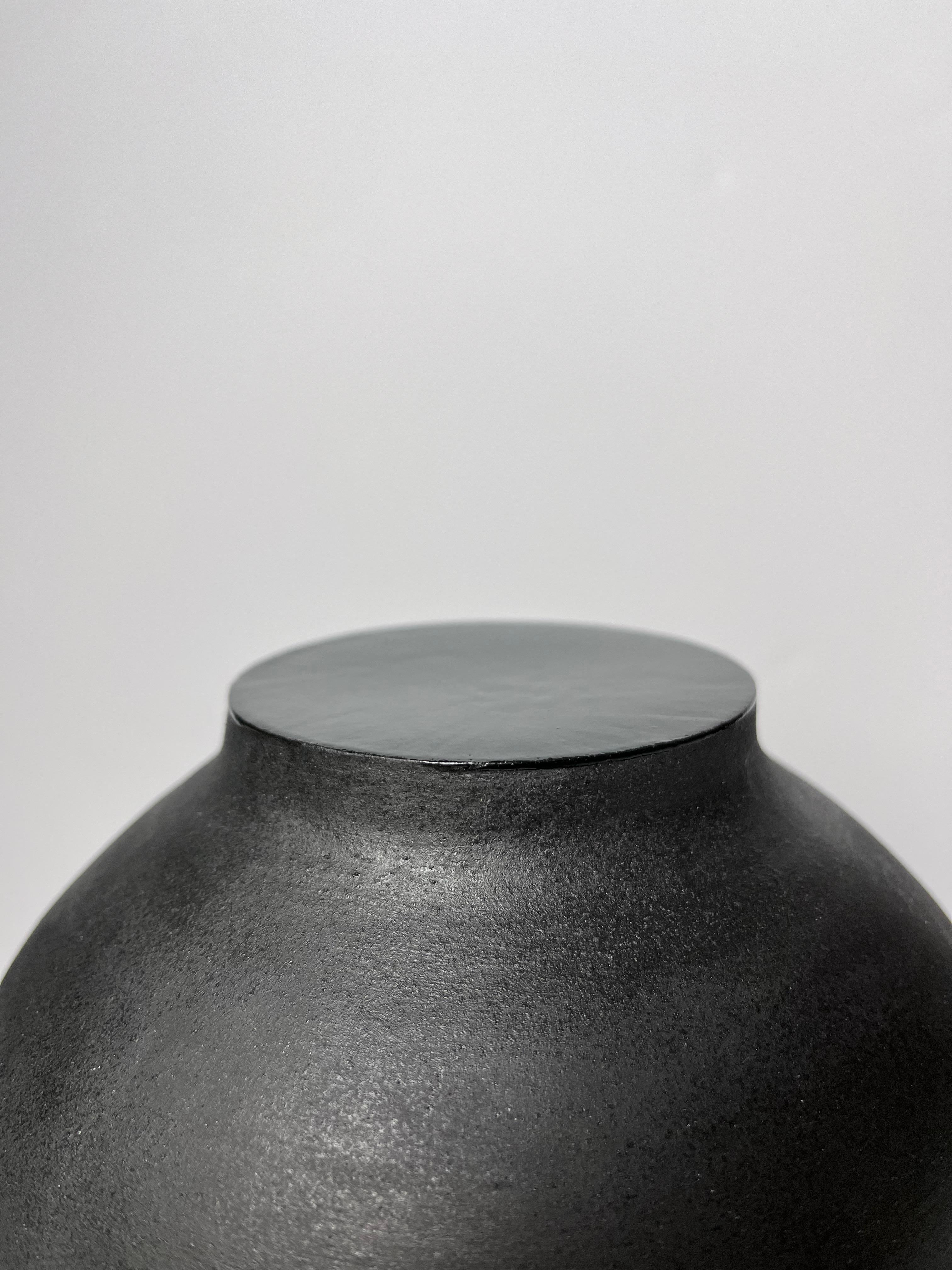 Vase en grès noir avec ouverture centrale et intérieur en grès gris ciment. La partie supérieure du col est fermée par un émail noir.
Entièrement fait à la main.