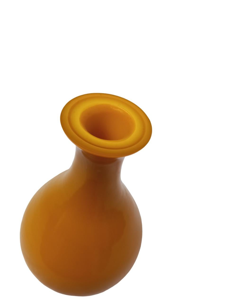 Vase en verre au profil doux et harmonieux, caractérisé par une silhouette en goutte d'eau se terminant par un col légèrement évasé. La couleur ocre jaune, chaude et intense, confère à l'objet une présence lumineuse et raffinée. La surface brillante