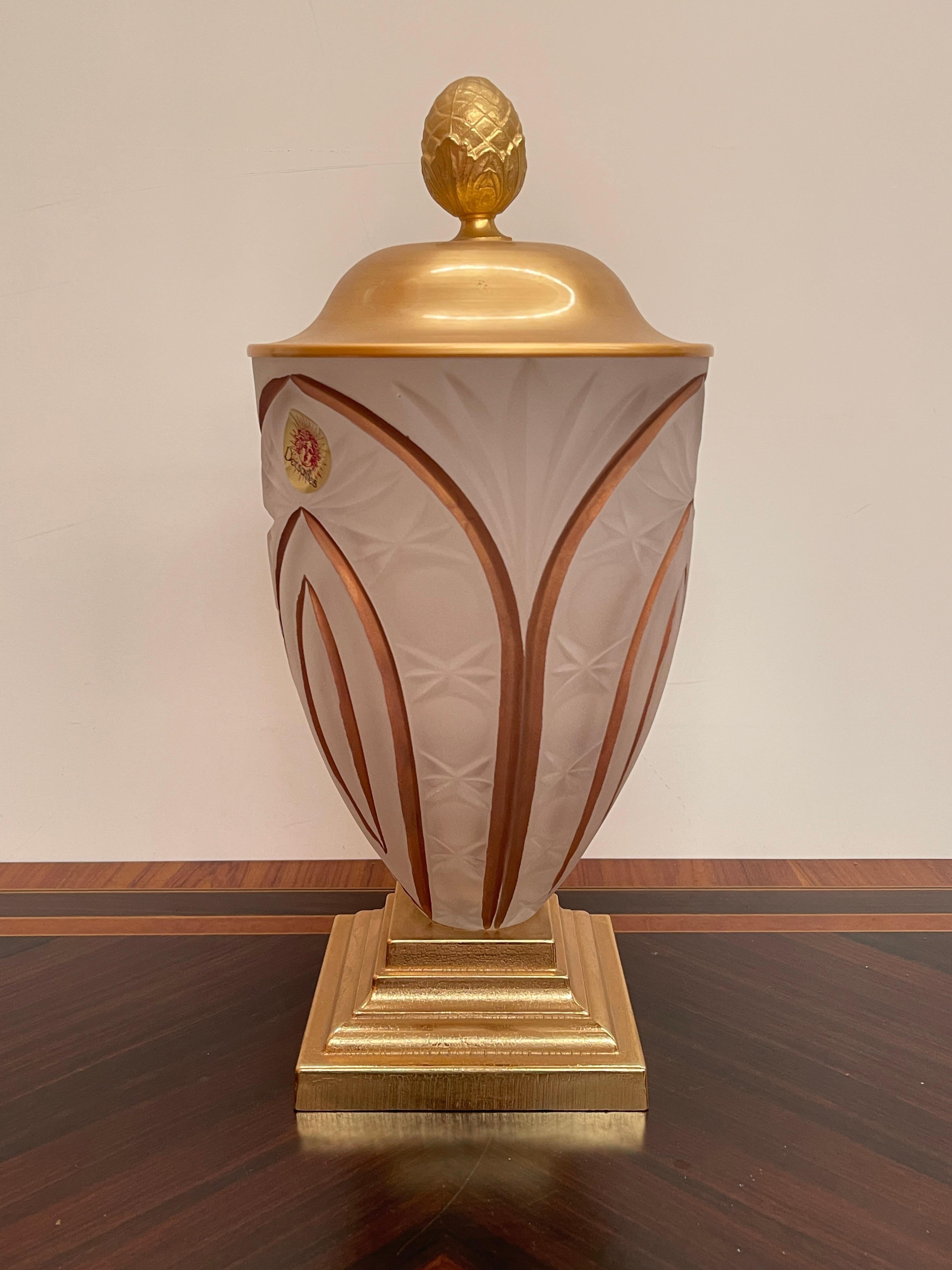 Eine elegante Vase aus satiniertem Kristall, die mit zarten Gravuren verziert ist, die ein Spiel aus Licht und Schatten erzeugen. Die Vase wird von einem quadratischen, vergoldeten Sockel getragen, der ihre Raffinesse unterstreicht, während der