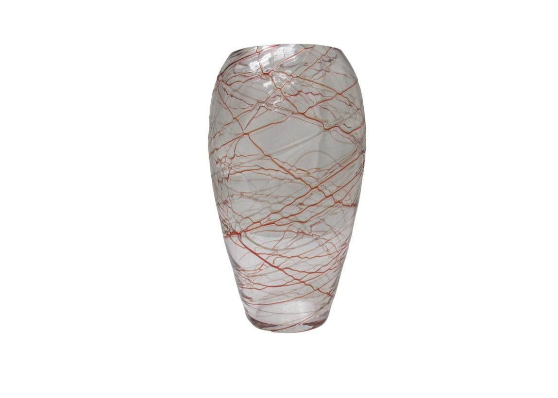 Elegante vaso in vetro soffiato, caratterizzato dall’inclusione di filamenti in lattimo nei toni del rosso e del grigio, di spessori differenti, che si intrecciano in un raffinato disegno a sviluppo verticale. La superficie e la trasparenza del