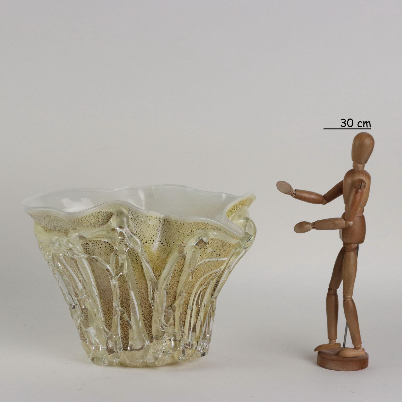 Vaso in vetro di forma irregolare nei toni del giallo con inclusioni in foglia oro e argento. Il corpo del vaso presenta fitte applicazioni in vetro trasparente a creare movimento. Sotto la base firma dell'artista e sul bordo etichetta adesiva della