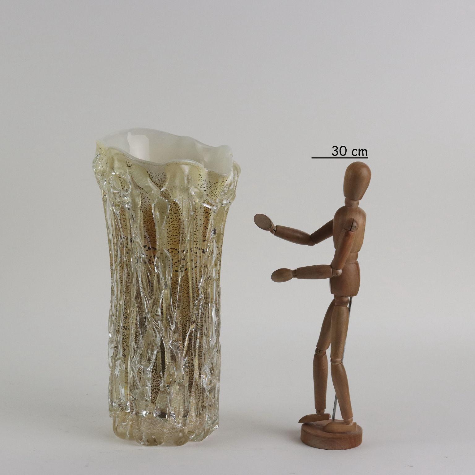 Vaso in vetro di forma irregolare nei toni del giallo con inclusioni in foglia oro e argento. Il corpo del vaso presenta fitte applicazioni in vetro trasparente a creare movimento. Sotto la base firma dell'artista e sul bordo etichetta adesiva della