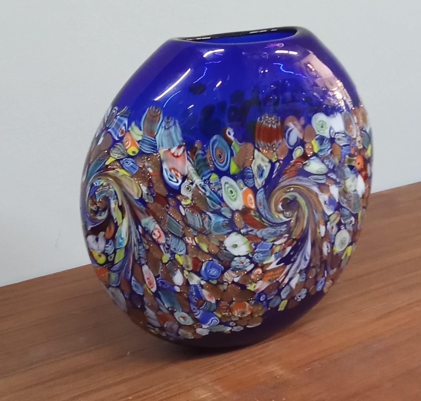 Schöne Vase  mit einem blauen Hintergrund mit einem mehrfarbigen abstrakten Muster, das eine auffällige Textur aus Formen und Farben erzeugt.
Vase aus Muranoglas (Venedig). Ca. 1980er Jahre.