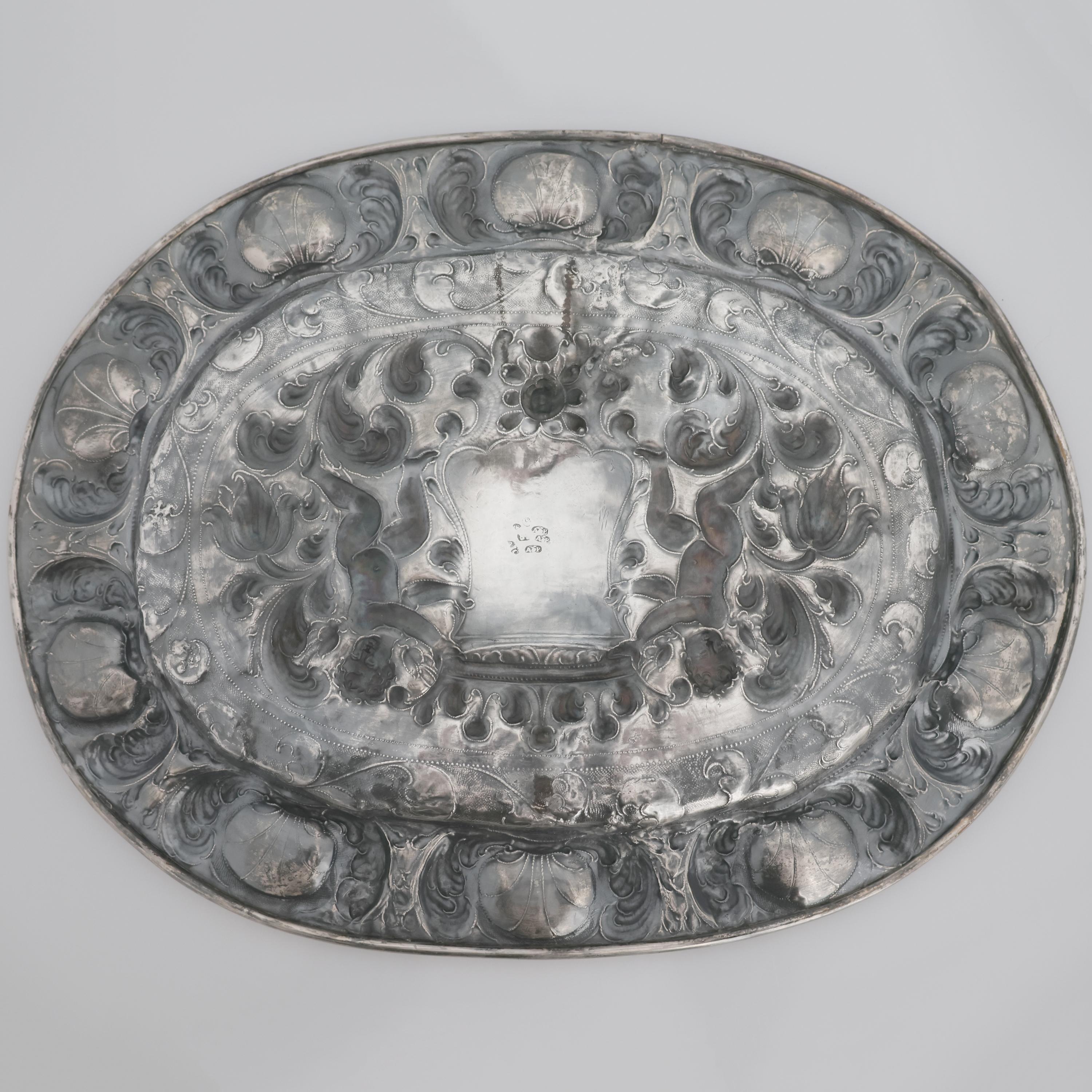 Beschreibung
Geprägtes und ziseliertes silbernes Parade-Tablett. Silberschmied Anzolo Castelli?, Prüfer Antonio Poma, Venedig, frühes 18
Zentraler Dekor mit zwei Putten, die ein gekröntes Wappen zwischen Pflanzenvoluten halten, Rand mit