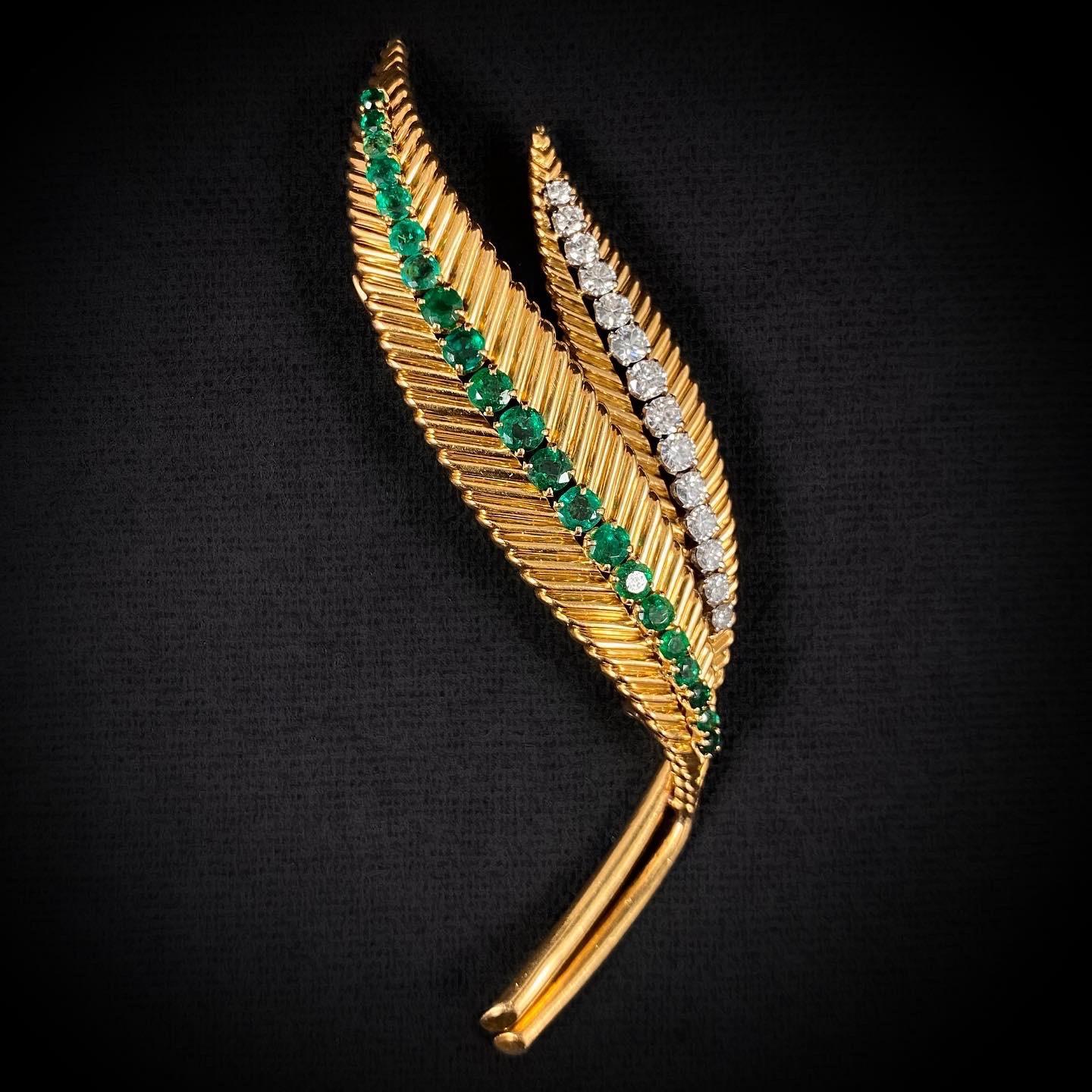 Van Cleef & Arpels diamond and emerald leaf brooch pin in 18 karat yellow gold and platinum, French, by Pery et Cie for VCA, 1960s/1970s. Modeled as two juxtaposed leaves with a fluted chevron pattern flowing through to a polished yellow gold stem,