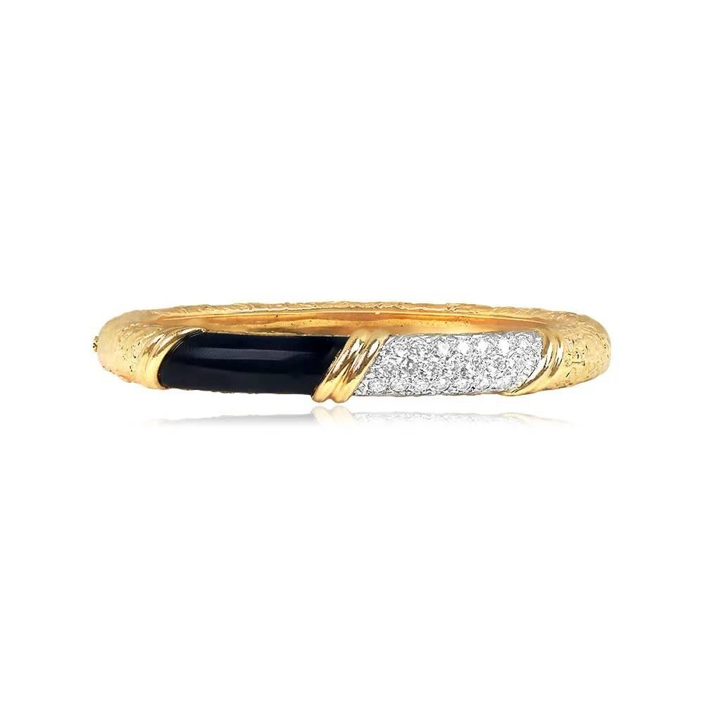 An exquisite Van Cleef & Arpels vintage bangle from the 1970s, showcasing a segment of onyx and pave-set diamonds. The bangle boasts a captivating textured gold design and is crafted in 18k yellow gold, signed VCA, and made in France.
The