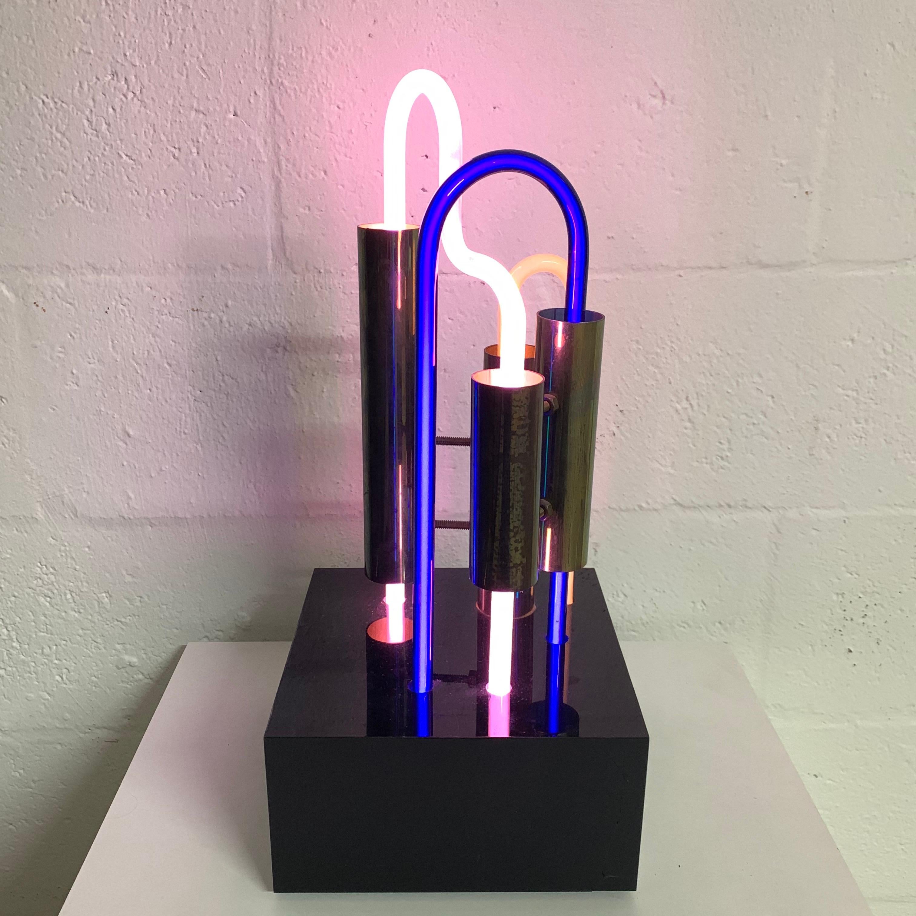 Postmodern table sculpture and or lamp rendered in blue pink, and white neon, with brass, on a black Lucite plexiglass base, designed by VCK, 1985, 32/200.