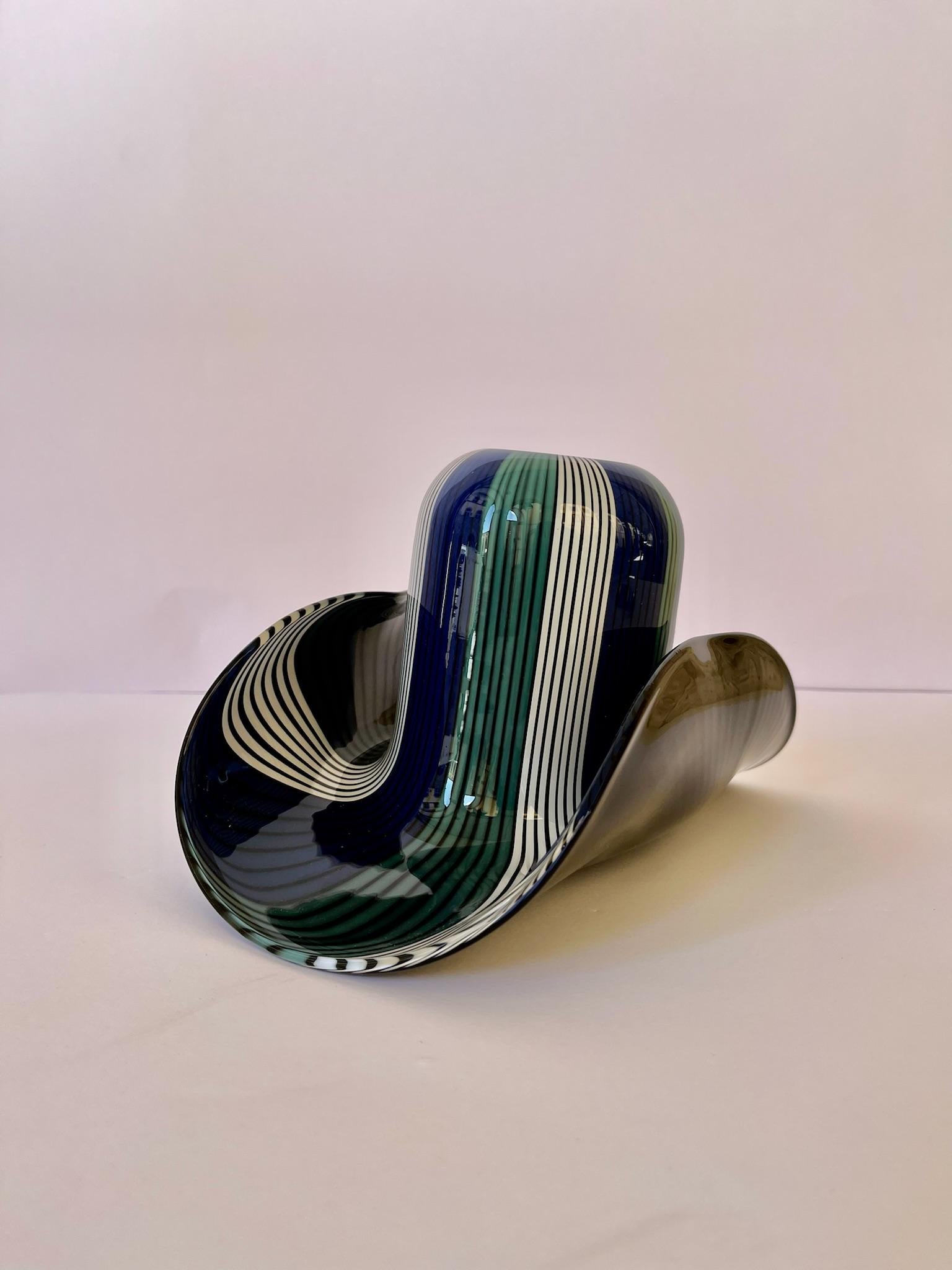 VeArt glass hat for Venini 1980.
This hat with the predominance of the color blue, white, and green is mainly used as a case if it is leaned in the smaller base and instead used as a decorative object in the larger base. However, it remains a vase