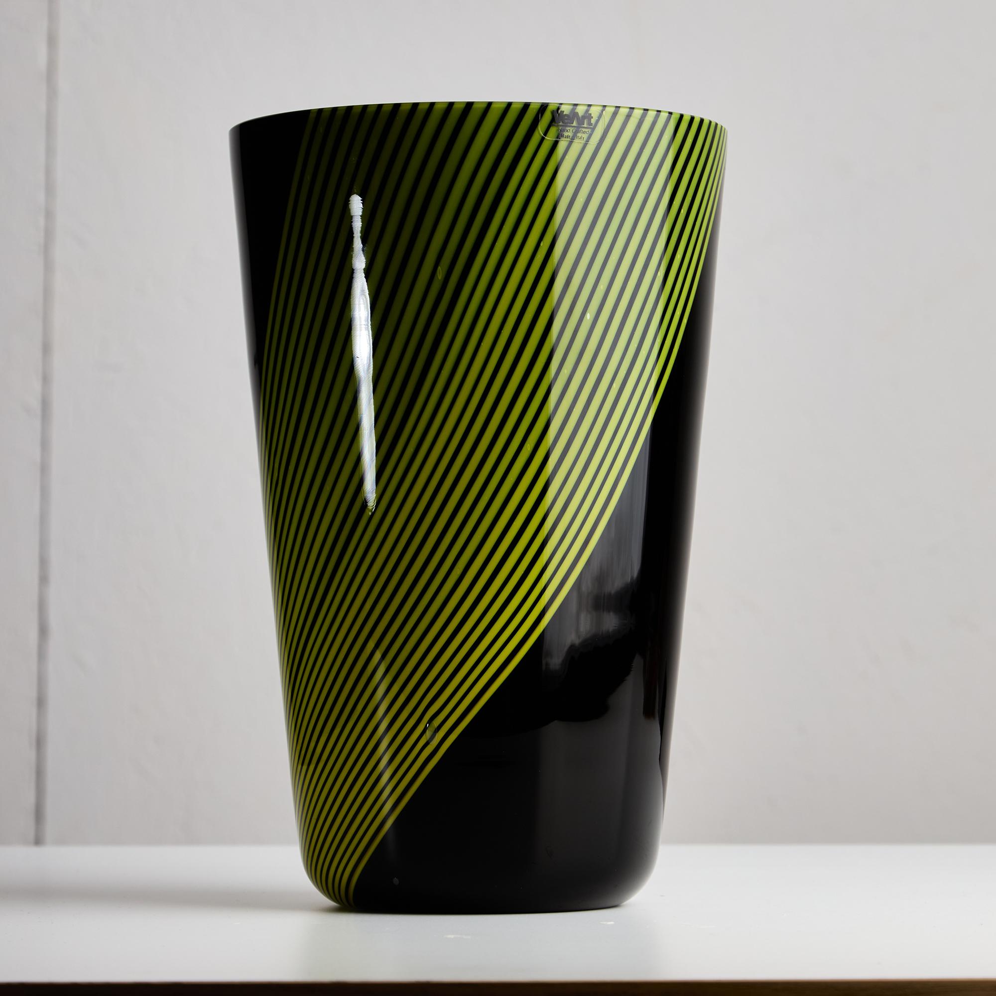Il Vaso in vetro di Murano VeArt del 1984 è un pezzo d'arte ipnotico che fonde senza sforzo eleganza e unicità. Ancorato da un'elegante base nera, il vaso mostra uno straordinario vortice di strisce verdi vivaci che danzano e turbinano dinamicamente