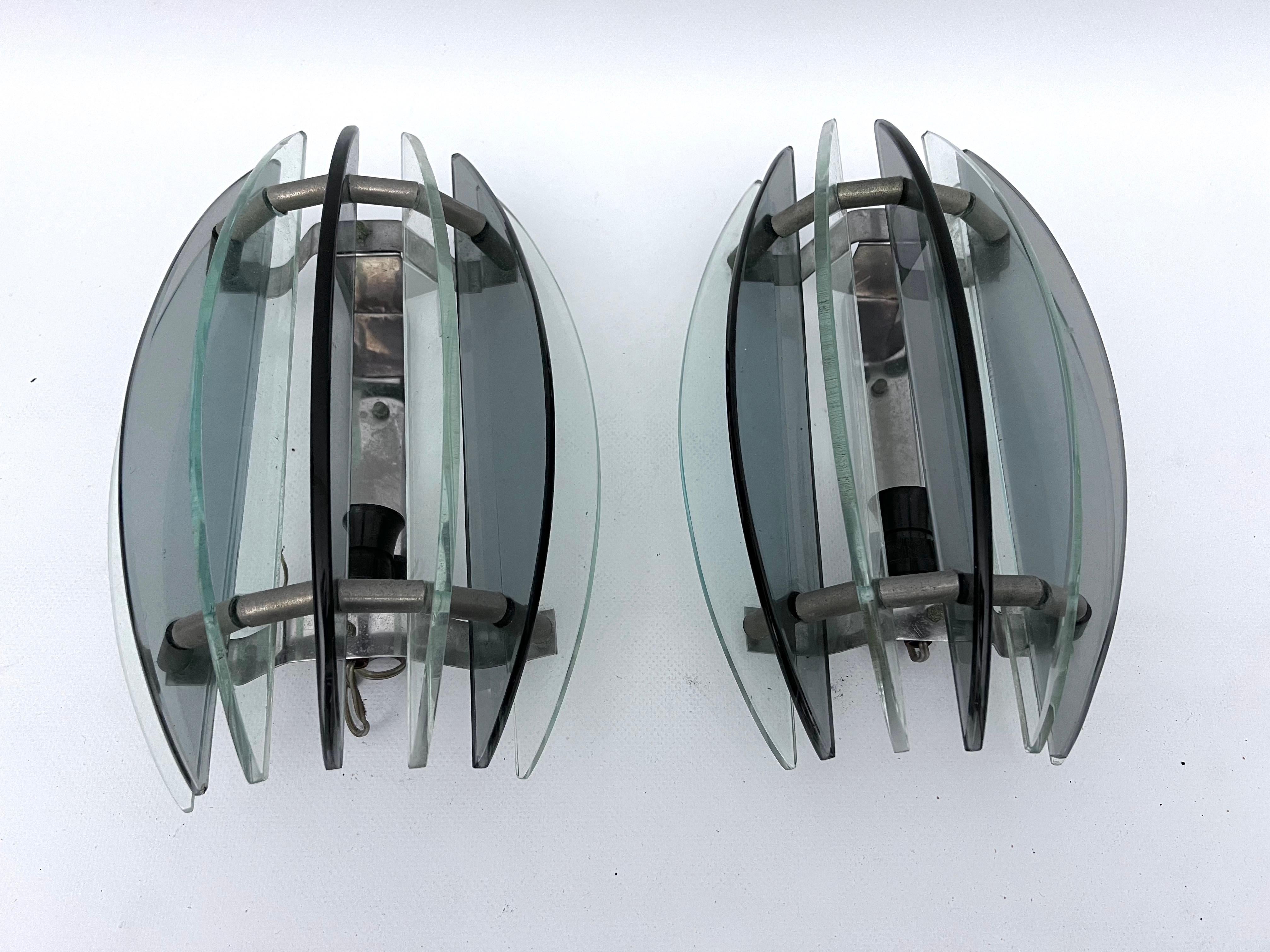 This pair of glass and chrome sconces have been produced from the Italian Veca during the 60s. Good vintage condition with trace of age and use. Some slight oxidation on the metal brackets. No chips or cracks. Full working with EU standard,
