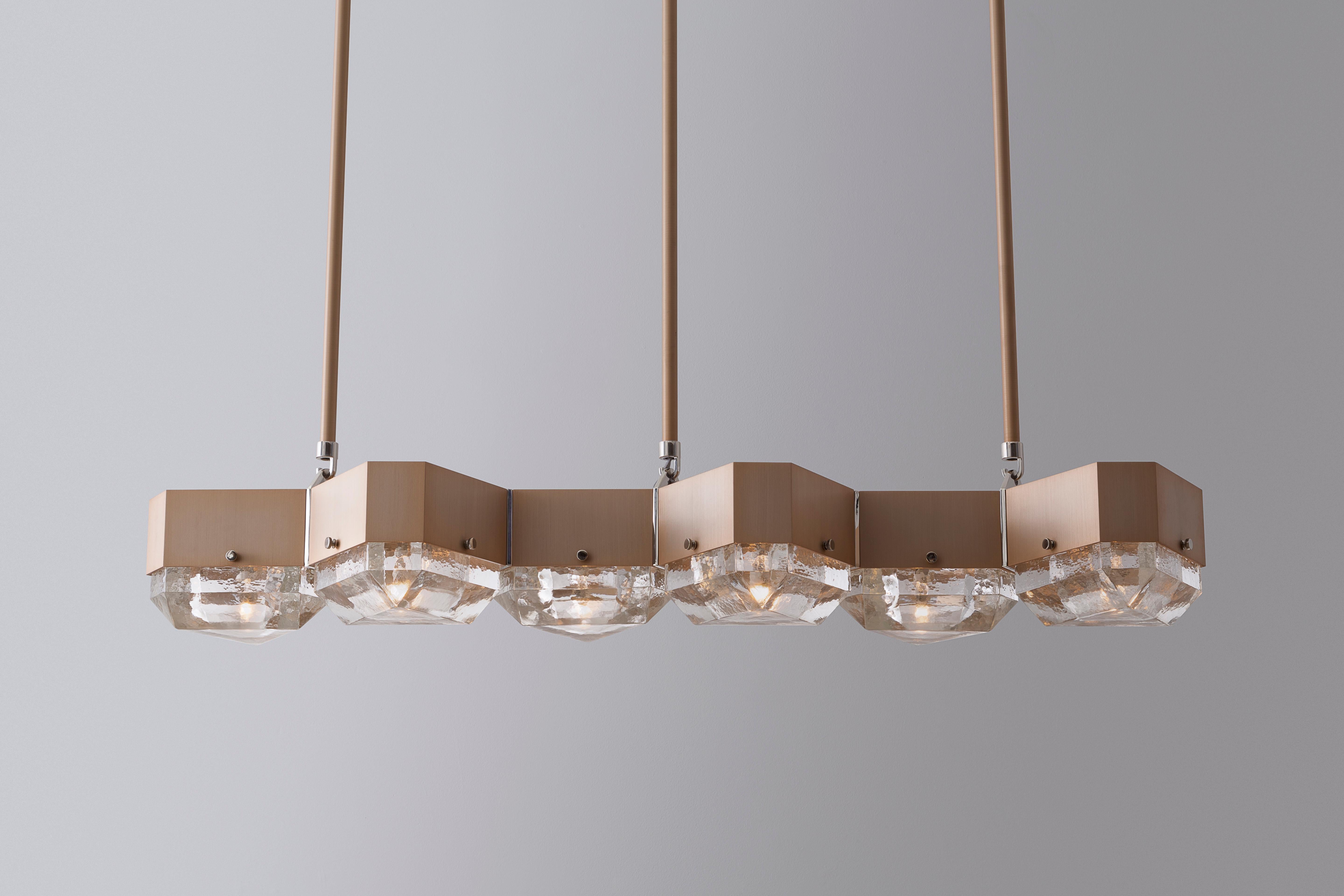 Vega chandelier is a modular lighting system fabricated from geometric metal components that support cast glass diffusers. Arranged in a linear form with a gold anodized body, polished nickel accents and cast glass diffusers. Lamping is shown in