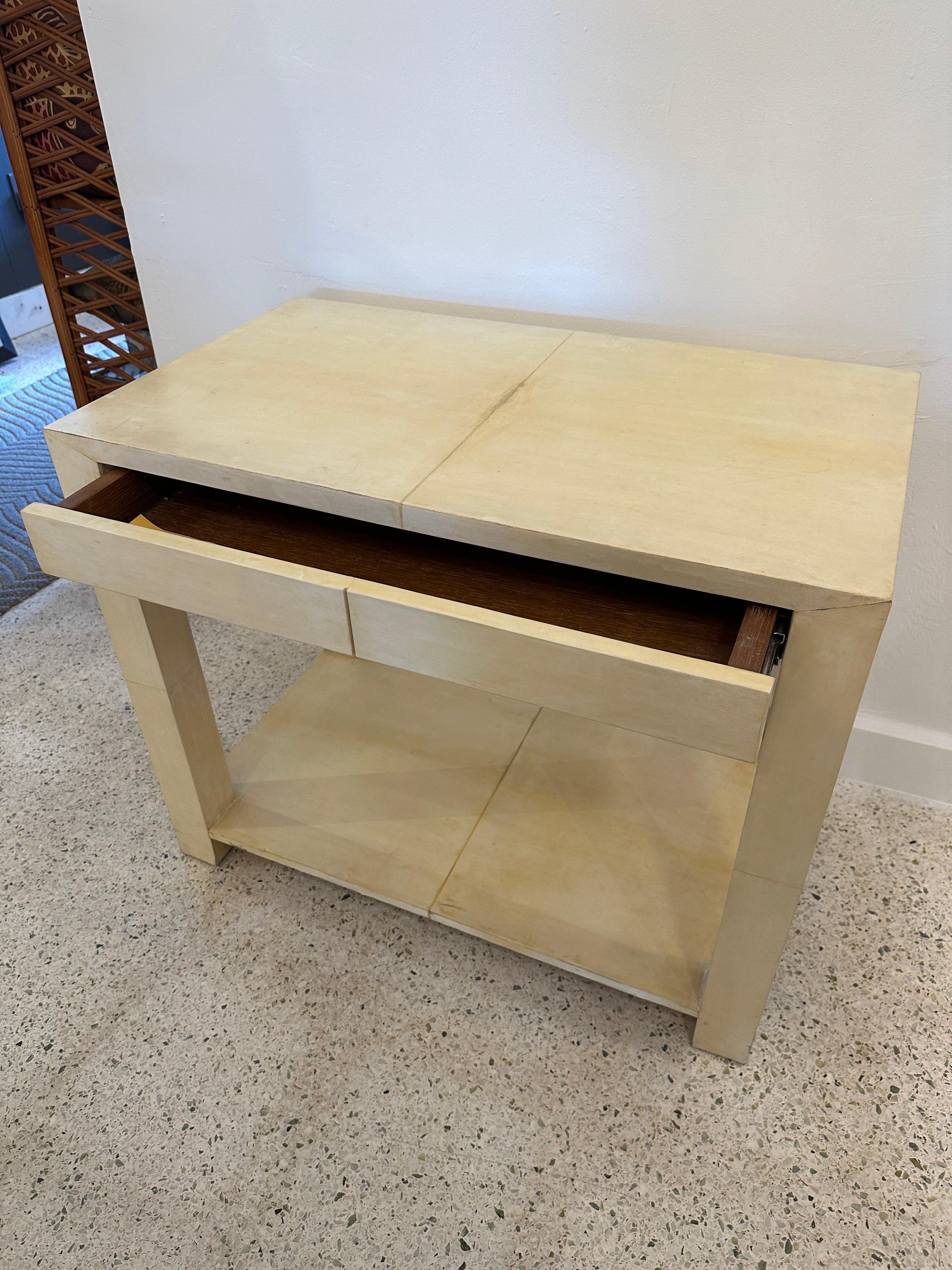 Very simple Parsons style table clad in vellum paper (parchment) with a hidden drawer and two tiers. Can be used as nightstand or foyer piece. Completely covered in vellum parchment with minor discoloration in spots (see detail images) but very