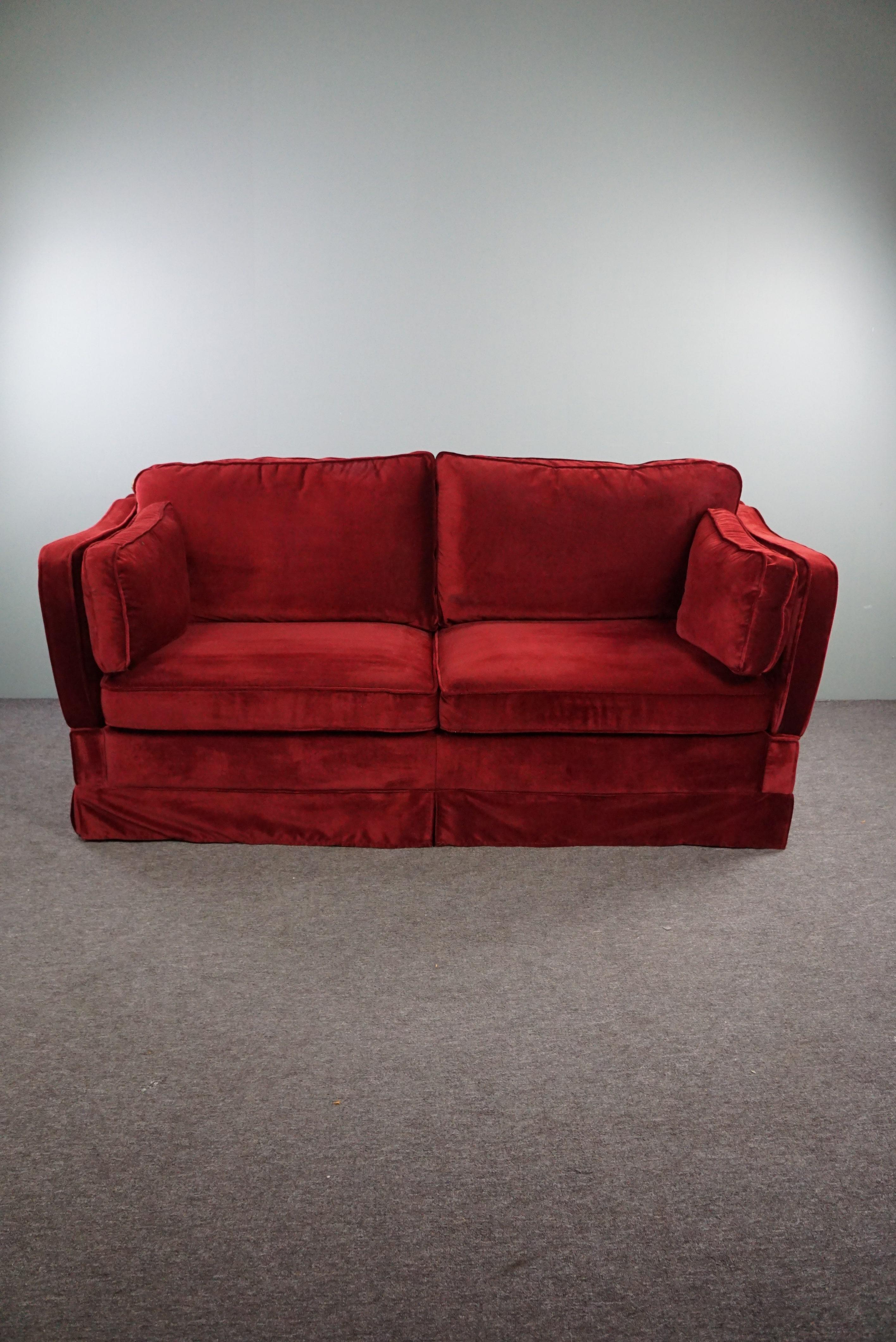 Offered is this velvet sofa with adjustable armrests in a beautiful deep red color.

With its deep red color and adjustable armrests, this sofa is a striking item. Place it in the middle of a room or against a wall where there is space to adjust the