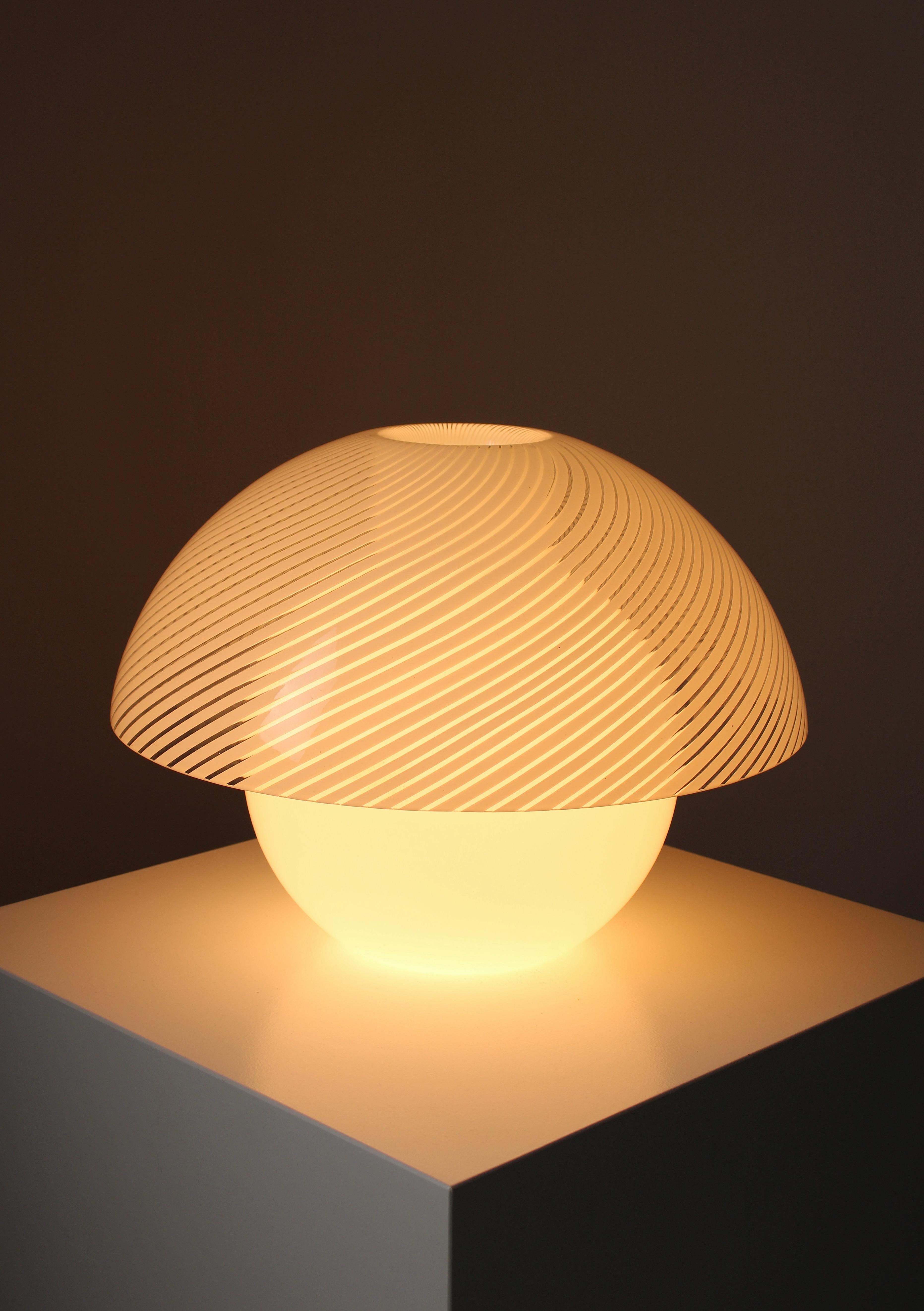 Large table lamp named VeloUno, consisting of two parts in Murano glass. At the bottom is a glass ball that serves as the base of the lamp and also provides support for the shade, which features a white swirl texture. This lamp was made by Milanese