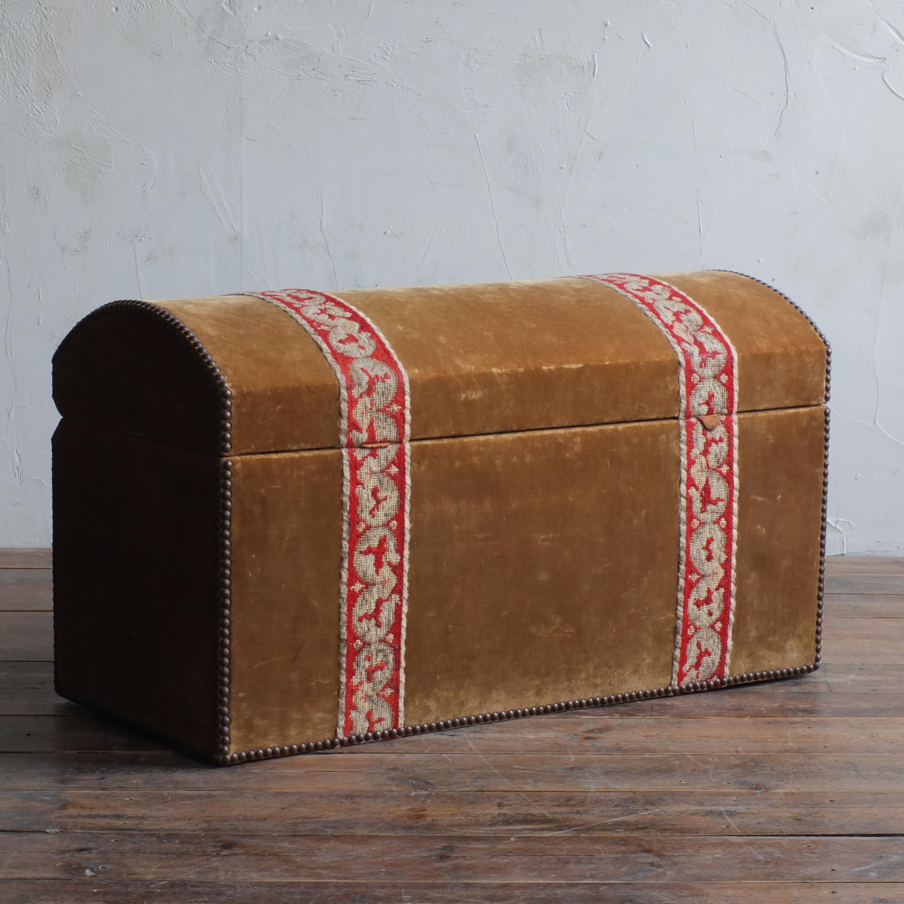 A very country house domed top trunk upholstered in worn gold velvet and red tapestry borders finished with brass studs. 

Measures: 90cm wide

41cm deep

51cm high.