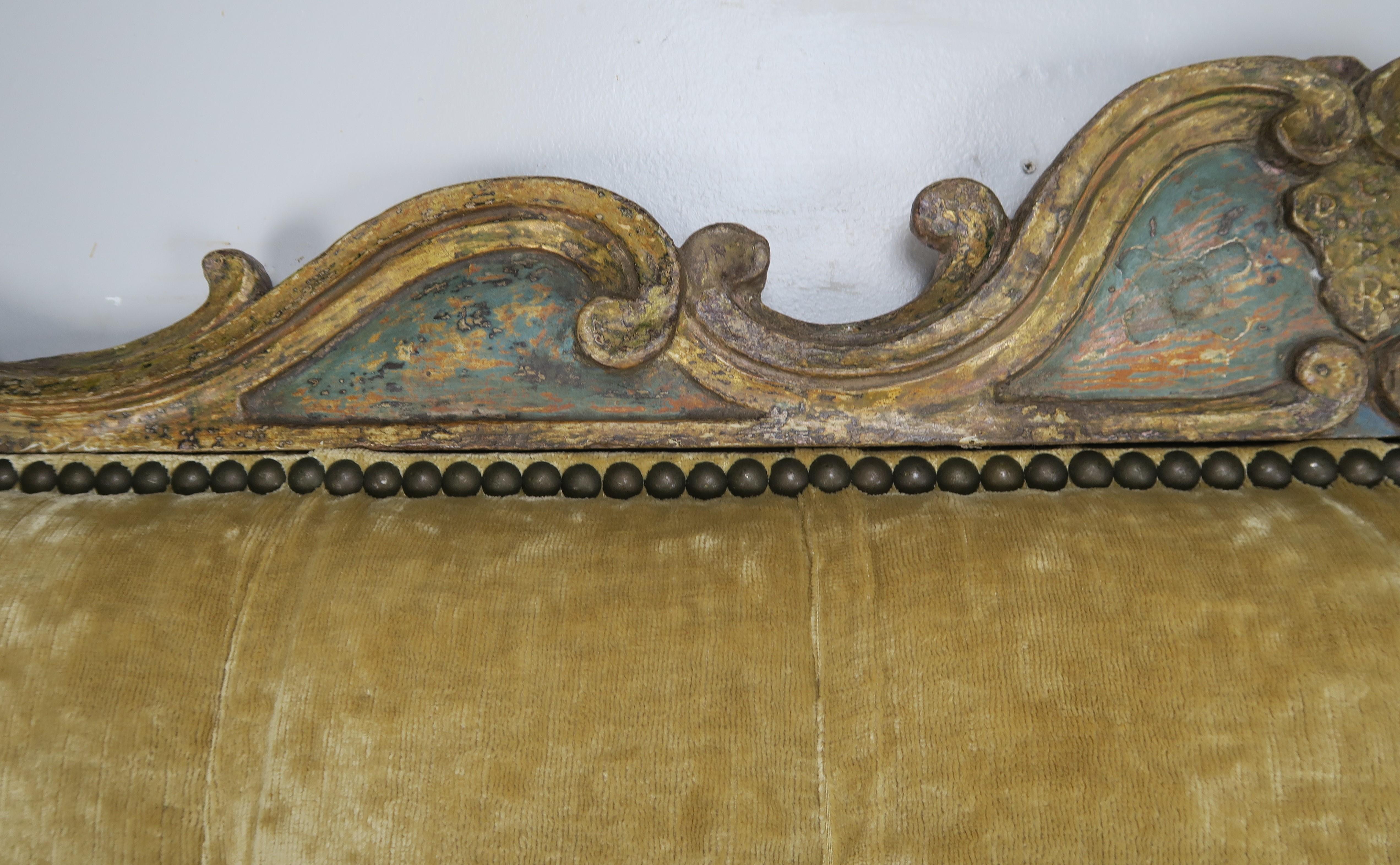 Custom king size headboard upholstered with a golden colored linen tufted velvet and finished with a 19th century Italian painted carving at top of the headboard. Also detailed with antique brass colored nailhead trim.