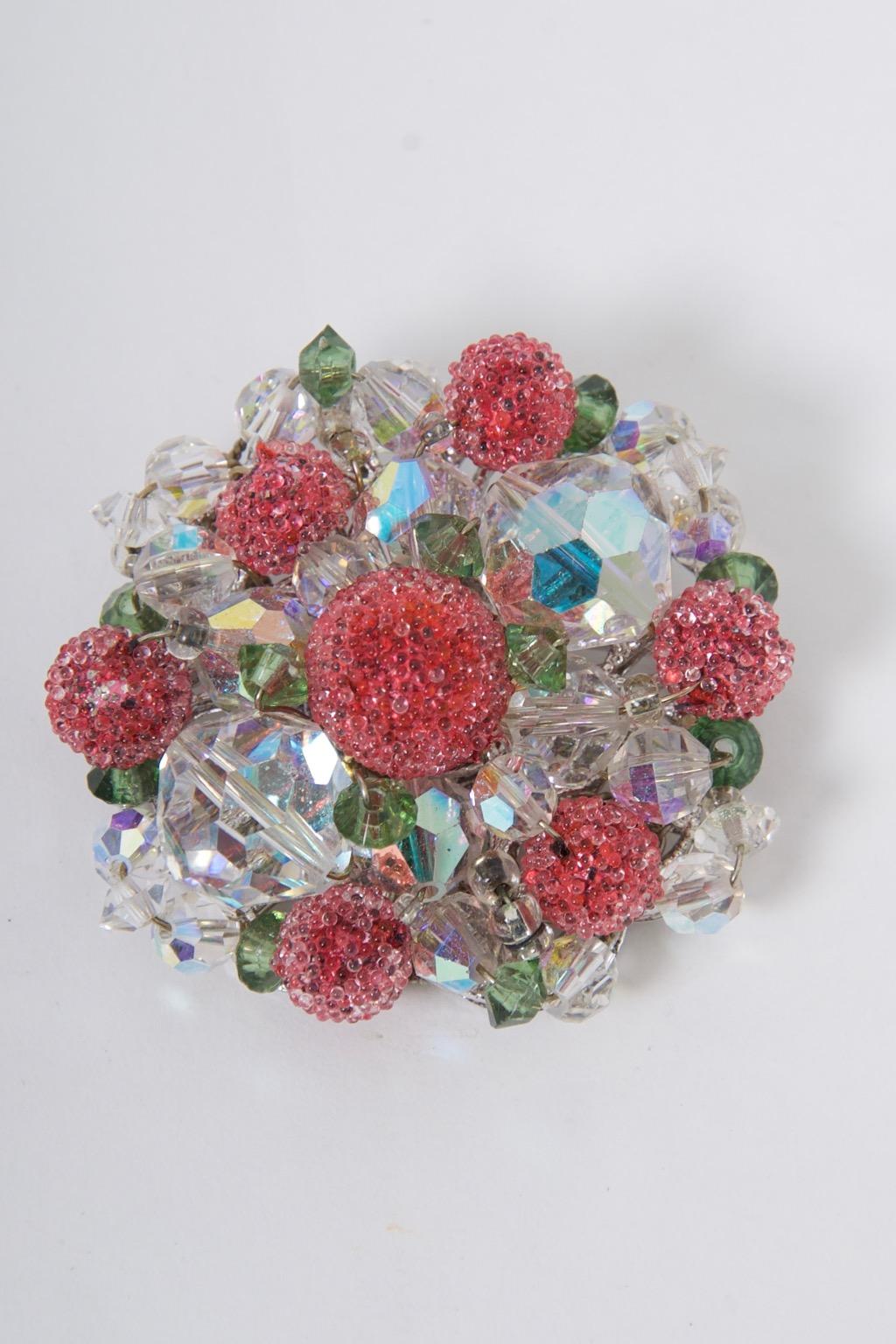 Vendome parure comprising a brooch, bracelet, and earrings, each composed of aurora borealis and green crystals of varying sizes, and each accented by spheres covered with coral mini beads evocative of flowers in bloom. The brooch has a silver tone