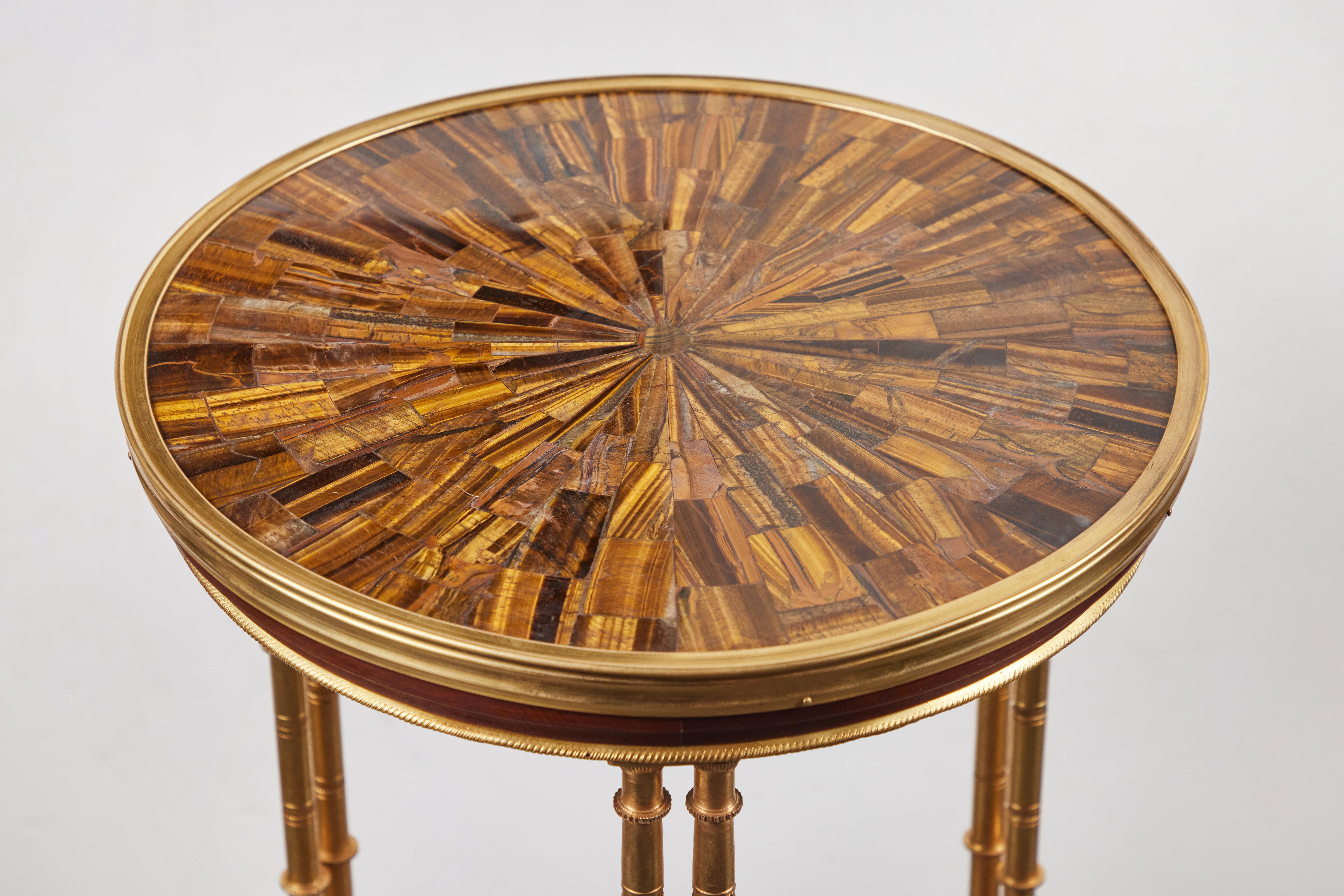 An elegant pair of veneered side tables with tiered pairs of gilt brass columns, and trim, and feet in the same. Each inlaid with luxurious, radiating, polished tigers eye gemstone tops.