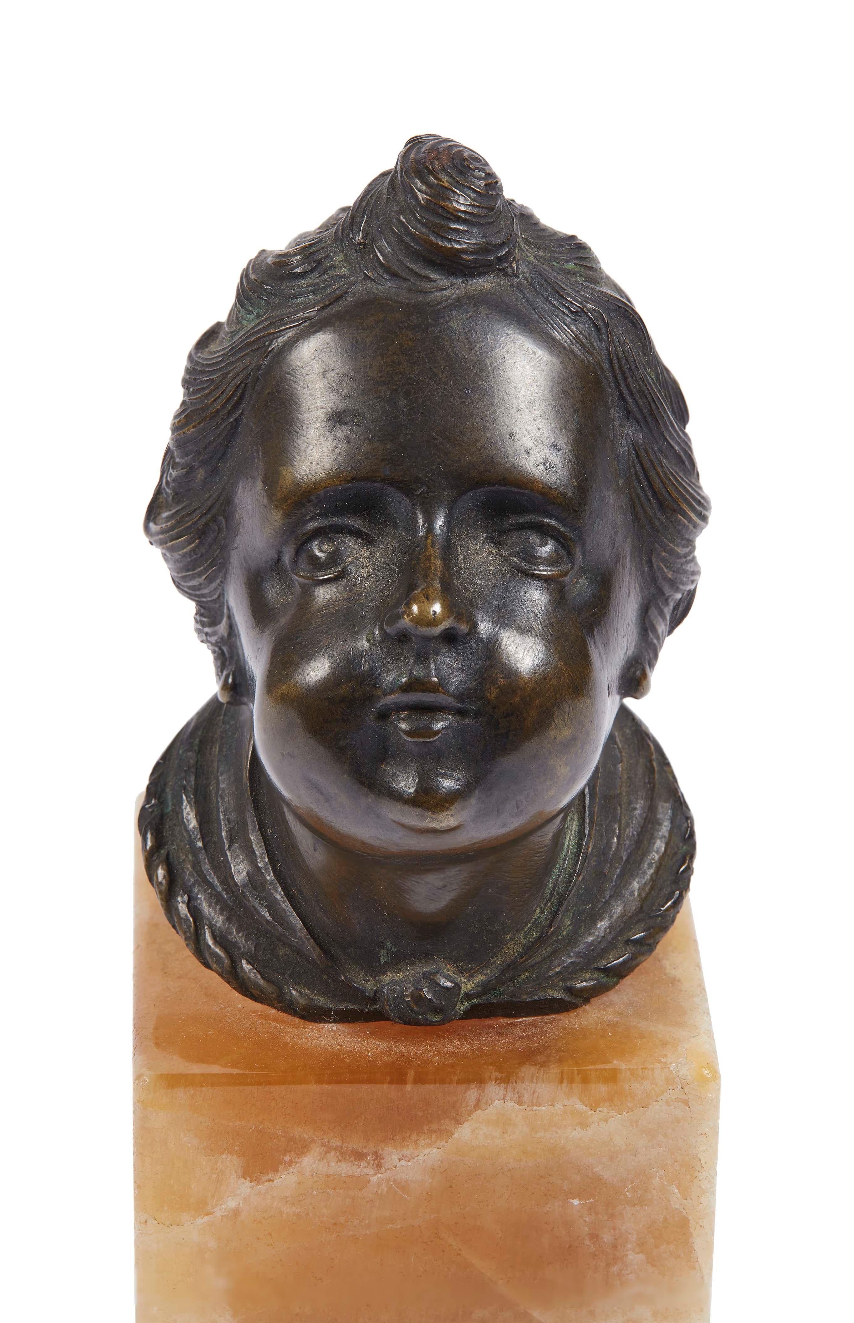 Réalisé en bronze en forme de visage de putto, 8 x 5,5 x 5 cm, sur une base parallélépipédique en albâtre non-pertinent, 9,6 x 5 x 5 cm.