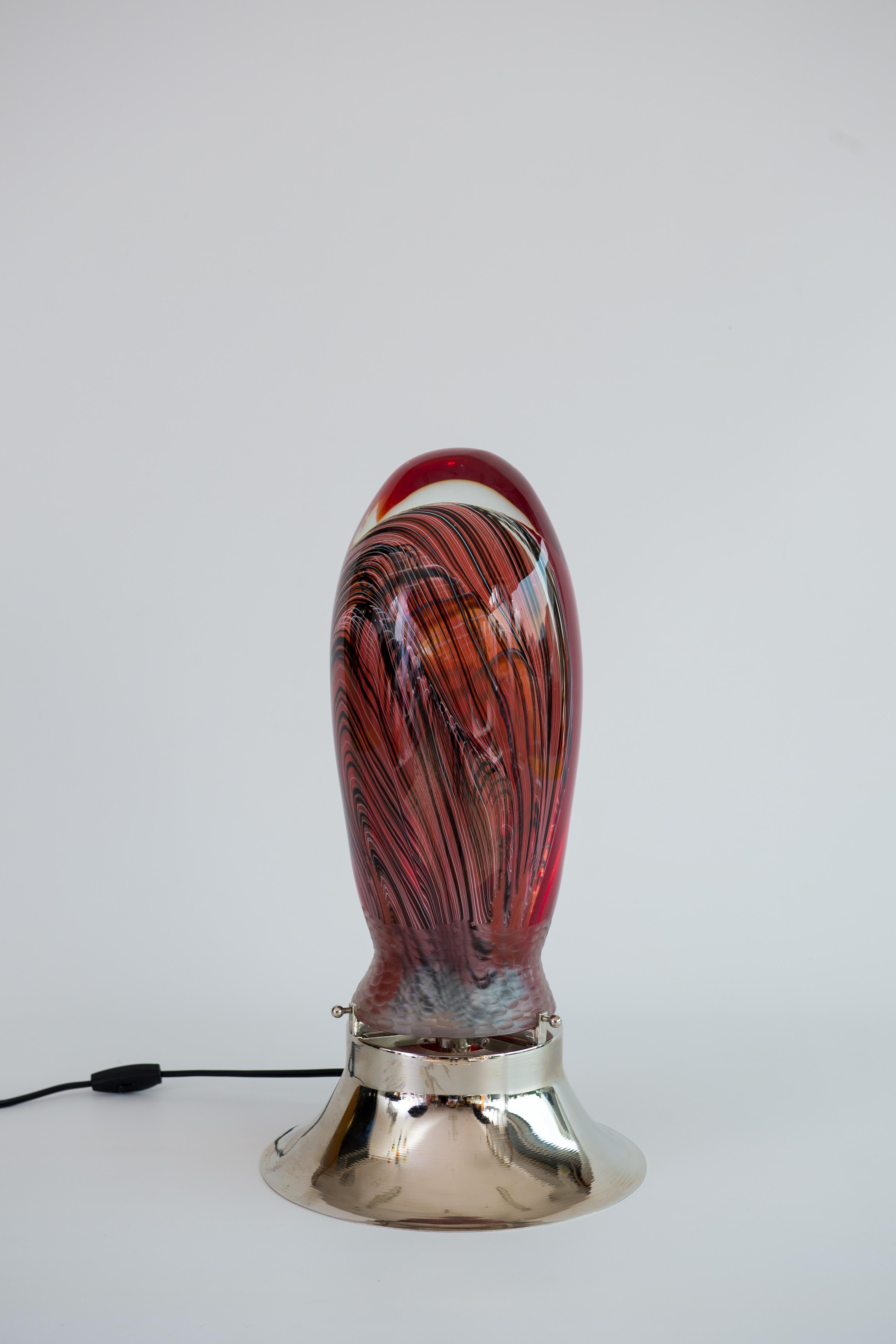 Abstrakte venezianische Tischleuchte aus mundgeblasenem Murano-Glas mit versenkten Filigranen, 1990er Jahre.
Dieses fantastische Kunstwerk ist eine schöne Glasskulptur, aber es ist auch so viel mehr, dank eines brillanten Lichts in seinem Inneren,