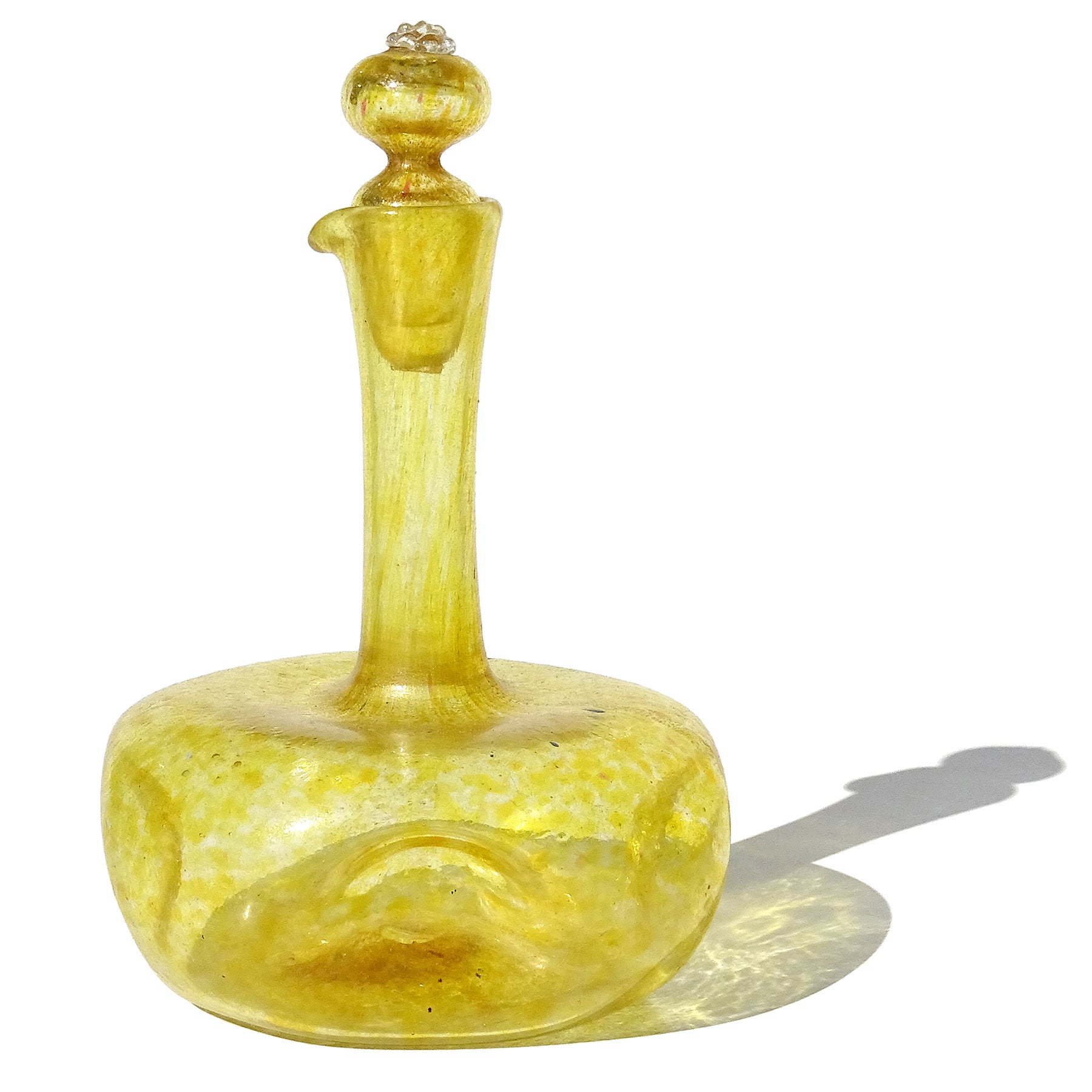Magnifique burette en verre d'art italien soufflé à la main, jaune et mouchetures d'or, avec bouchon d'origine. Attribué à la serre de la Compagnia Di Venezia E Murano (C.V.M.). La bouteille a une forme arrondie, mais alvéolée de chaque côté, ce qui