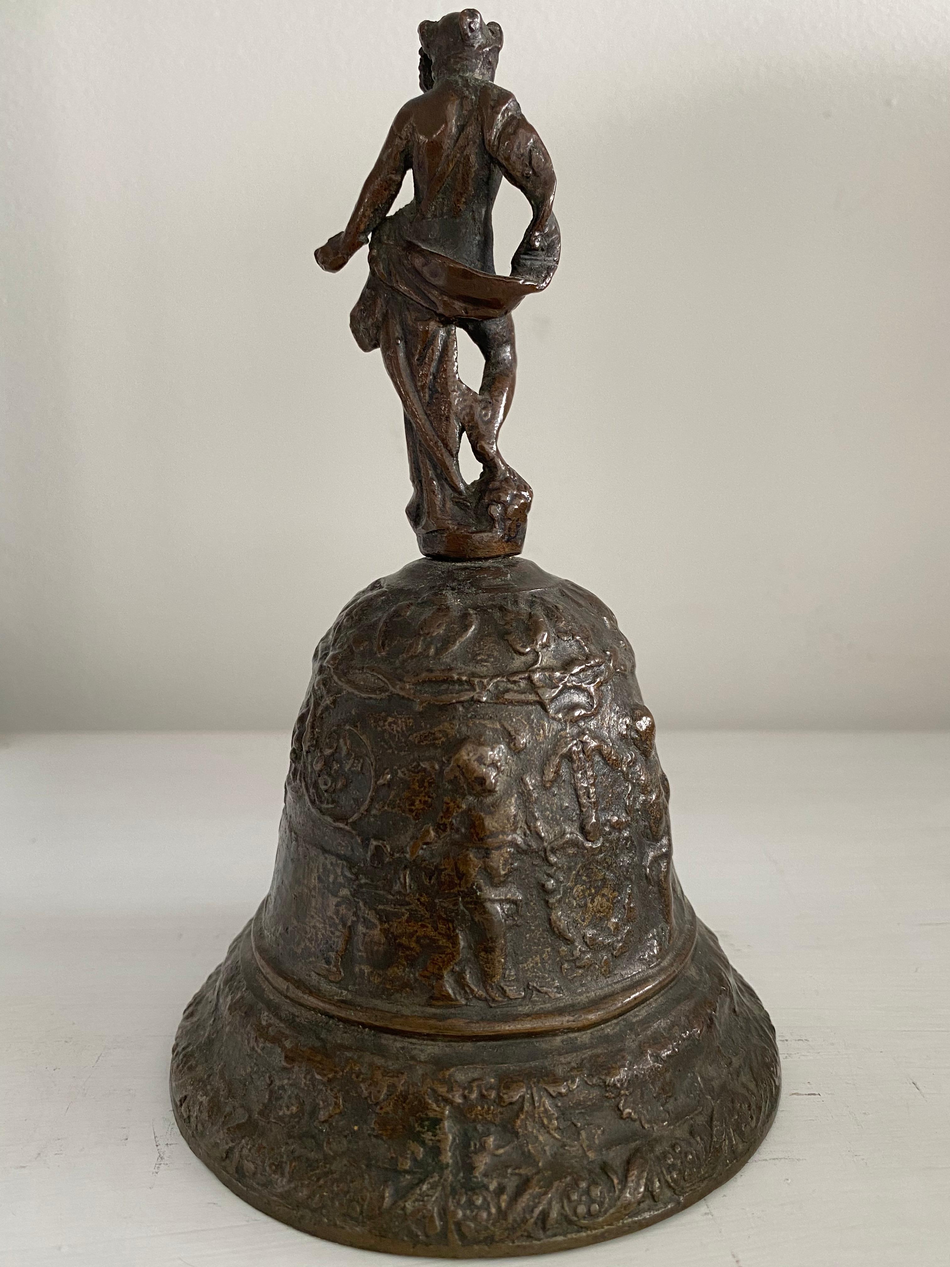 This bronze bell is of the type cast in Venice in the 16th century. It is topped with a figure of Mercury surmounting a procession of putti with garlands and a blank cartouche. It measures 7