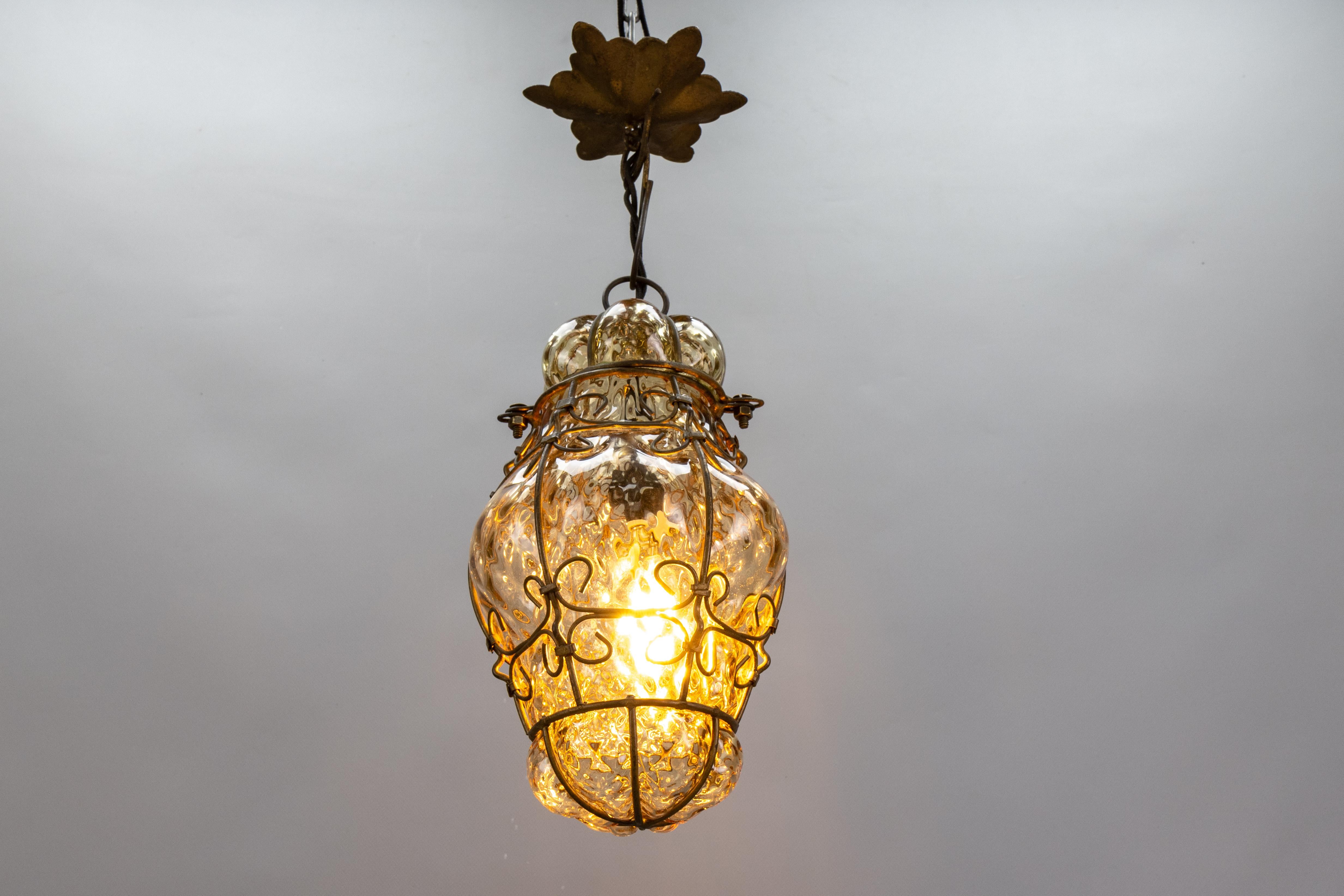 Venetian Caged Amber Toned Murano Glass Pendant Light Lantern, 1930s, Italy.

This exquisite Venetian caged Murano glass pendant lantern from the 1930s showcases the timeless elegance of hand-blown Murano craftsmanship. The blown glass body, with