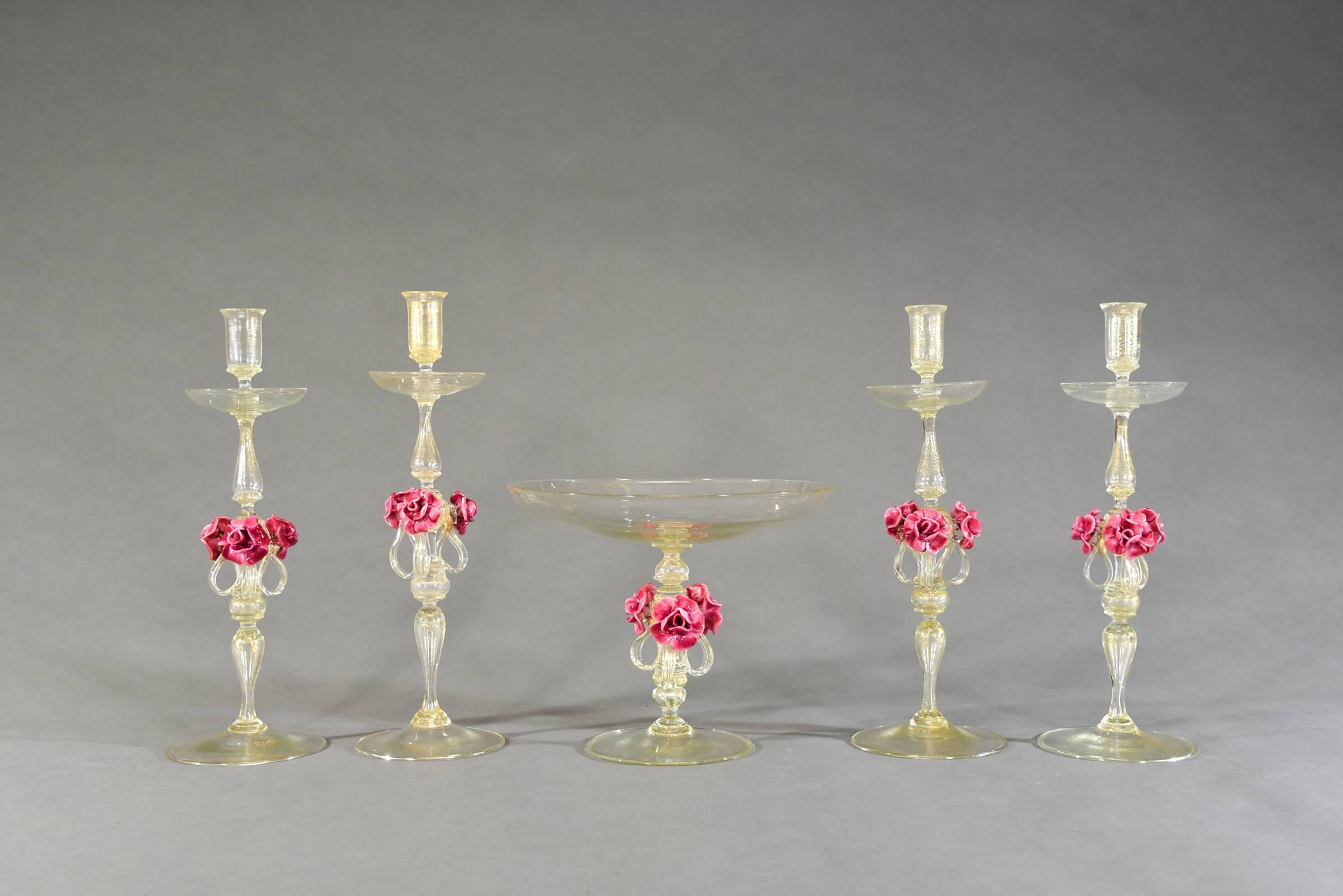 Attributed to Salviati, this set of four hand blown candlesticks and matching footed centerpiece, will be the focal point of any table setting. Filled with gold leaf inclusions, the glass blower has created a masterpiece set with applied roses and