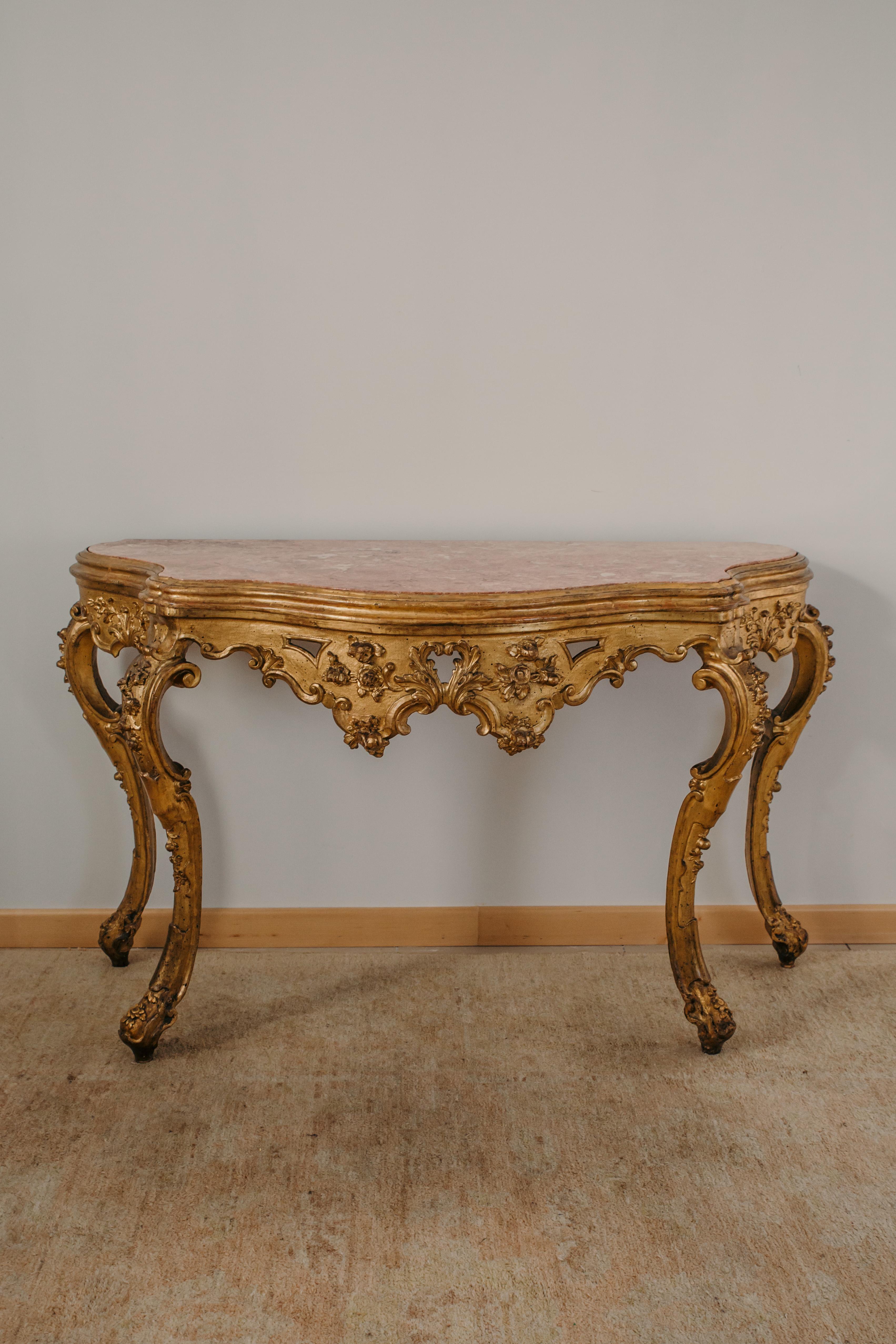 This console was made in the XVIII century in Venice, Italy, from carved and gilded wood. The recessed top is in pink marble. The console has a Louis XV style line, with a strongly shaped top, a band and curved legs. On the front and sides the band