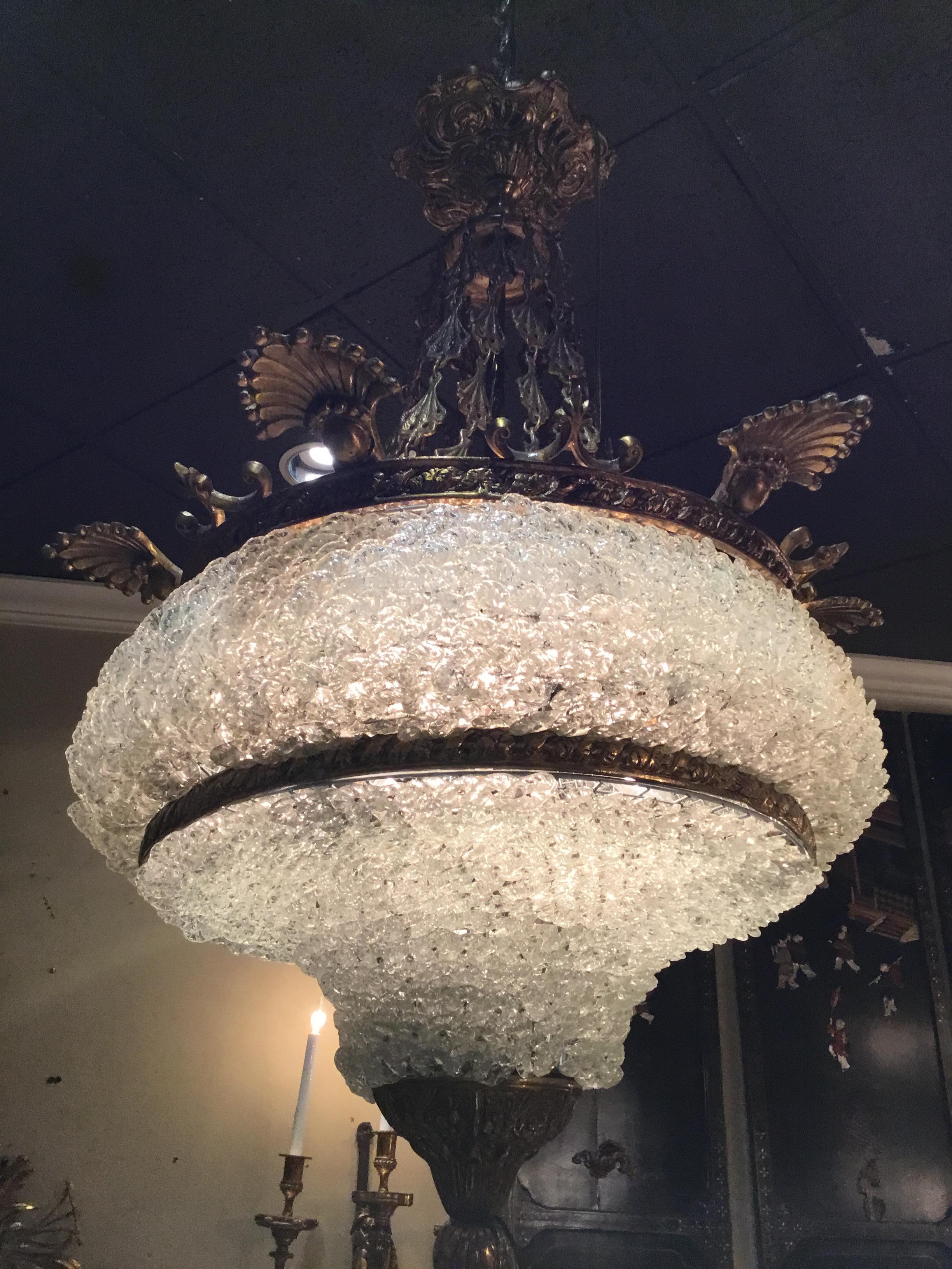 A bowl shaped fixture made up of a multitude of Venetian crystal pieces
That surround the fixture holding six lights. This combination creates
A beautiful diffused light. It is supported by antique bronzed chain.
It ends in a well cast bronze