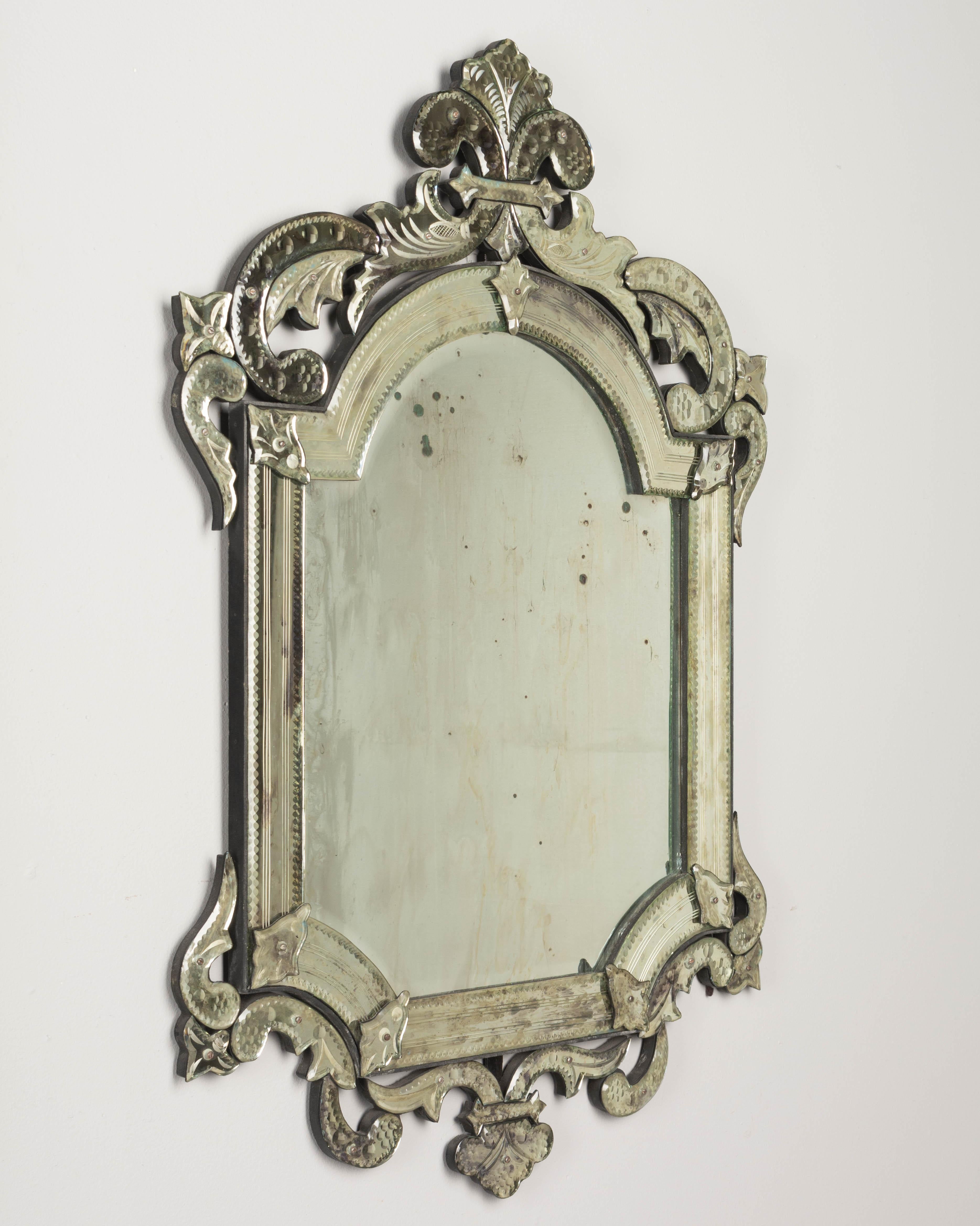A vintage Venetian mirror with several separate scroll shaped pieces that have been cut, beveled and etched. Fleur de lys crown. Original looking glass with old fogging and silvering. Mirror pieces affixed to black painted wood backing. Nice muted