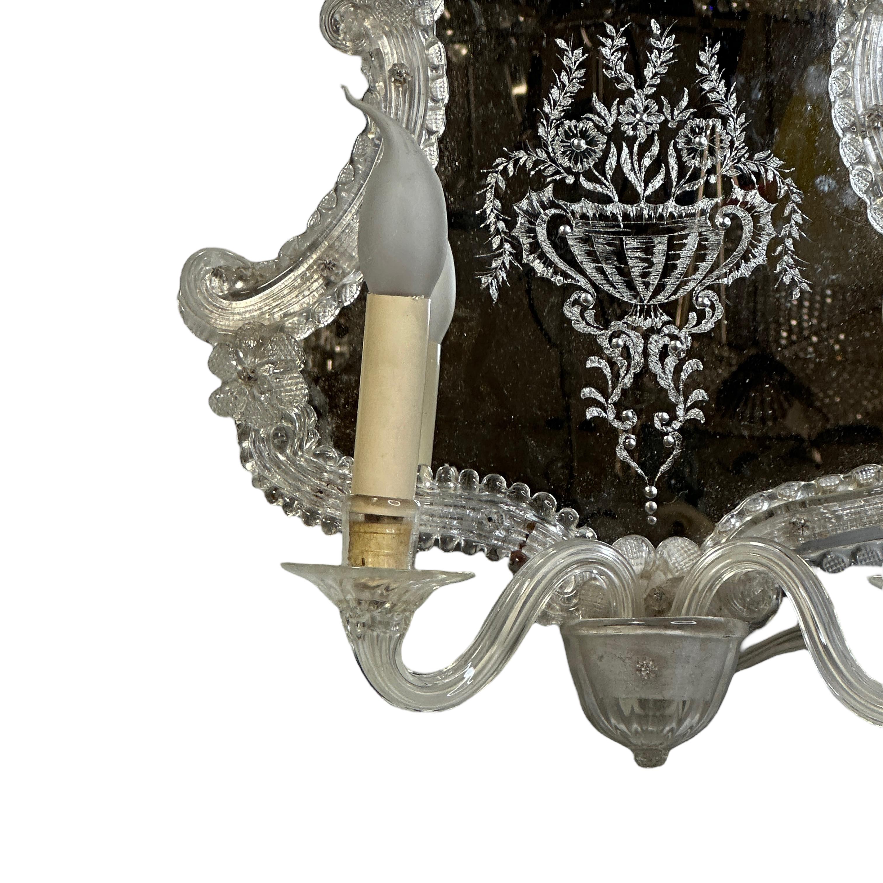 Vintage Italian Hollywood Regency style mirror wall sconce hand blown in clear Murano glass with decorative details, antiqued patina on mirror, mounted on wood back frame. The fixture requires two European E14 / 110 Volt candelabra bulbs, each bulb