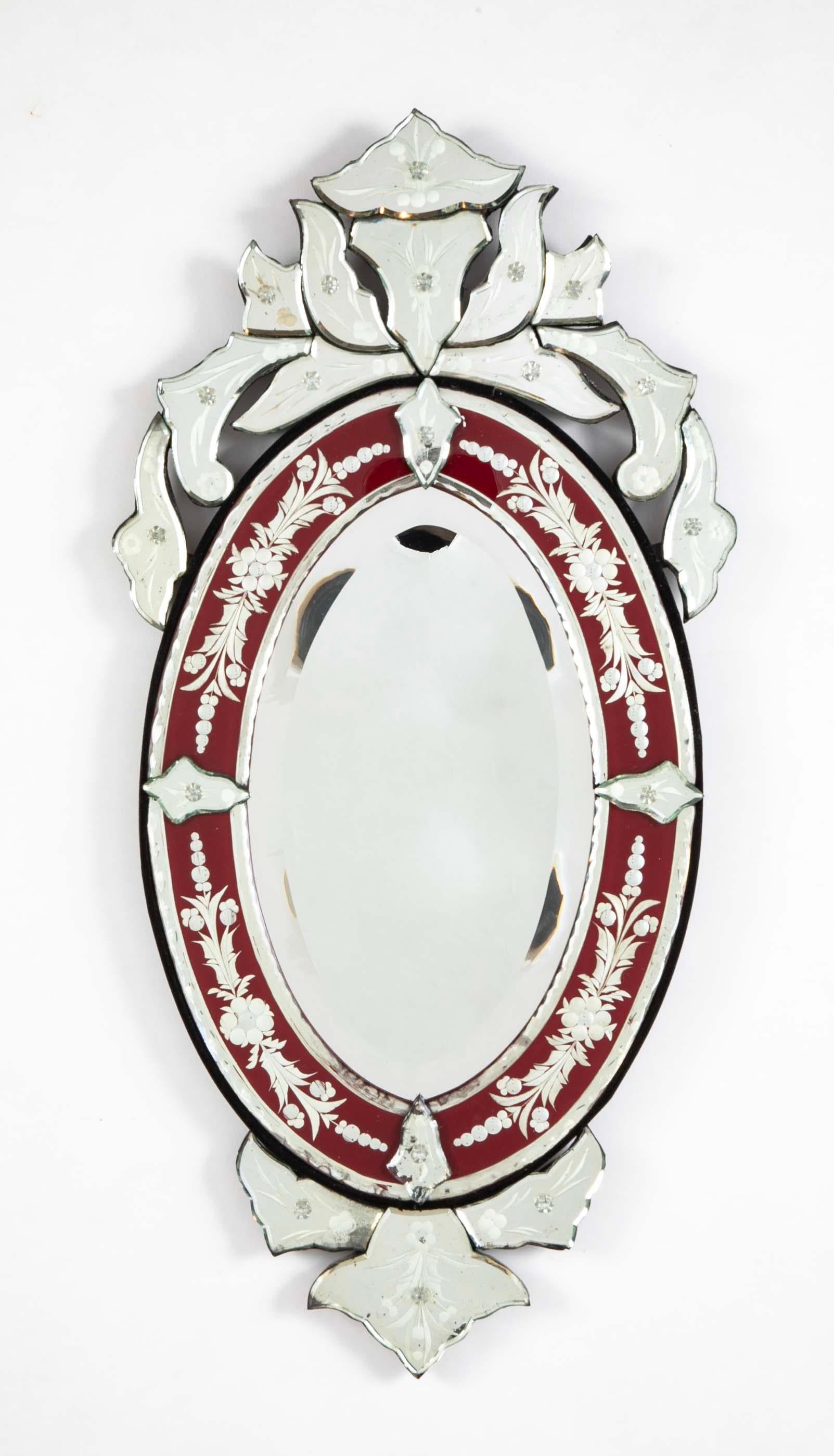 Ovaler Spiegel aus geätztem und abgeschrägtem venezianischem Glas mit roter Färbung. Im Rokokostil mit kunstvoller Krone aus geschliffenem und geätztem Glas. Eingefasst in einen ovalen Rahmen aus feinem schwarzen Samt. Ein schöner und auffälliger