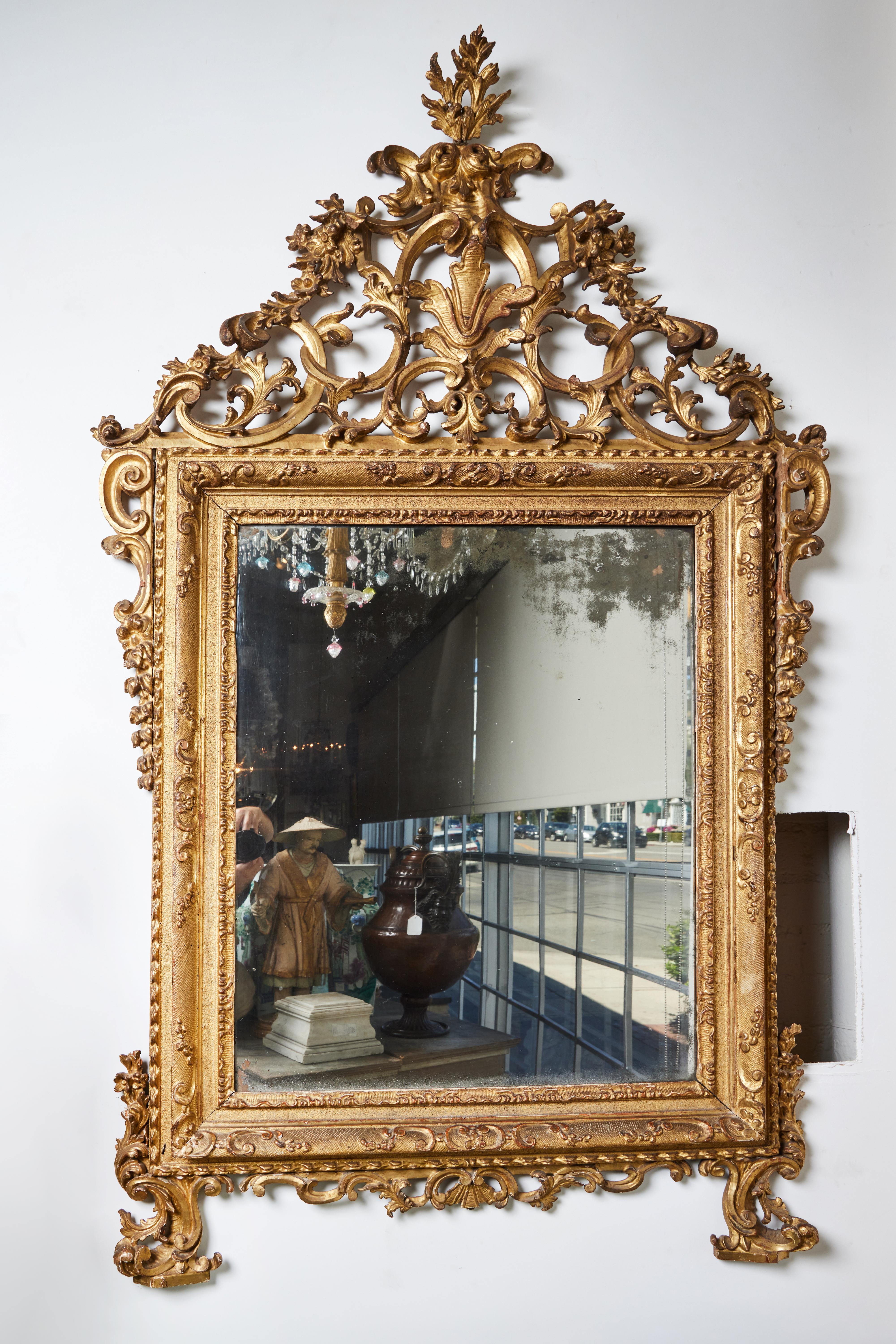 Un incroyable cadre vénitien, sculpté et doré à la main, avec un verre miroir d'origine qui a subi des pertes dues à l'âge. Couronne percée et feuillagée.