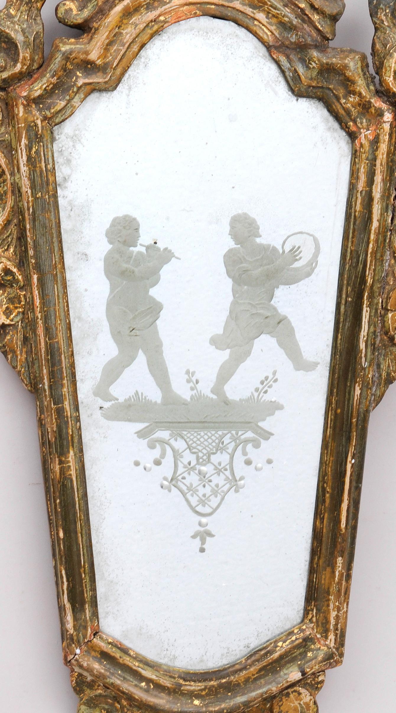 Venetian giltwood mirror with frame robustly carved with shell crest and both C-scroll and foliate borders enclosing a plate with engraved figures of marching musicians playing the flute and tambourine on a grassy patch, carved pendant below, some